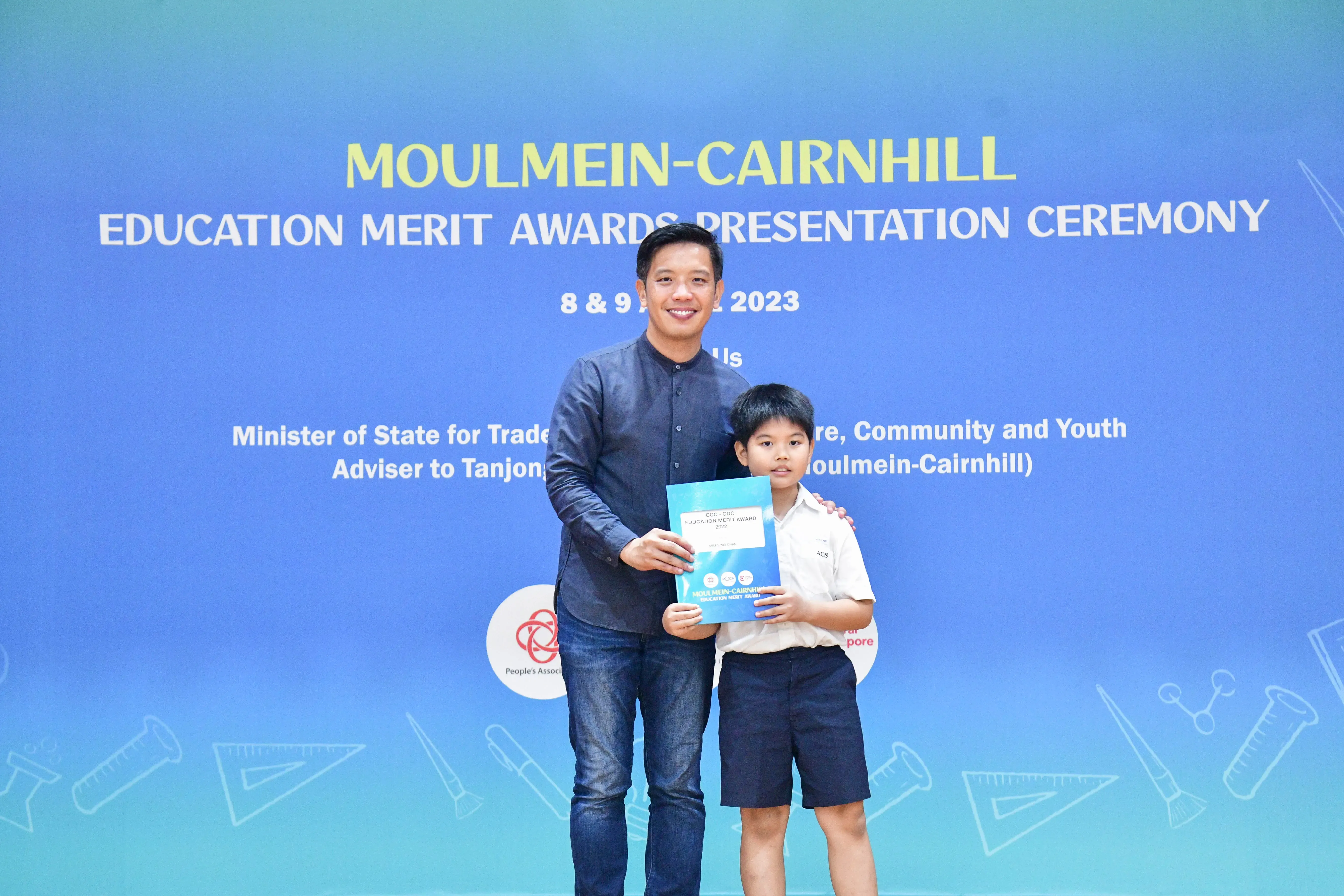 Man and young boy hold a certificate together at the Moulmein-Cairnhill Education Merit Awards Ceremony 2023.