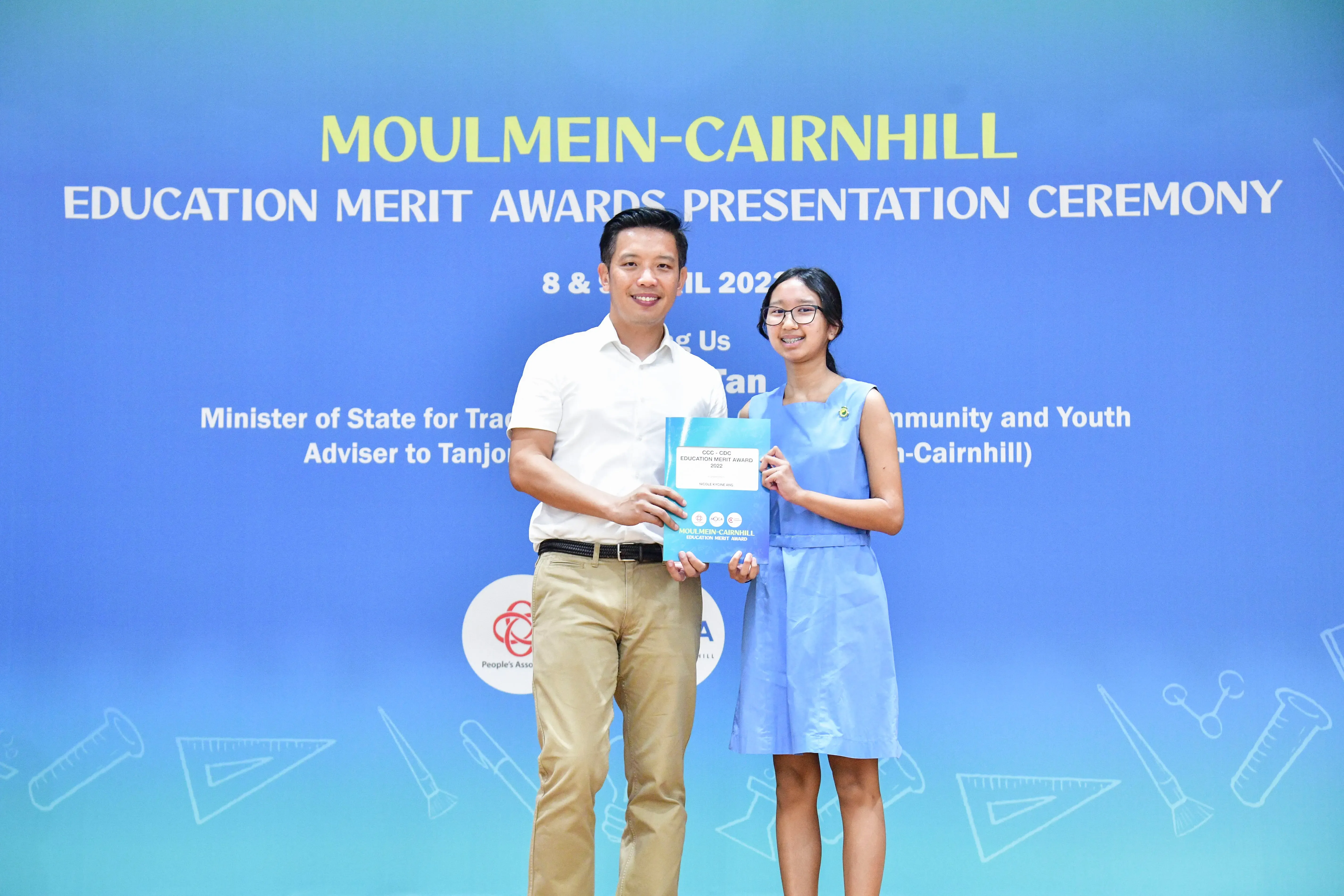 A man and a young girl hold an award certificate at the Moulmein-Cairnhill Education Merit Awards Presentation Ceremony.