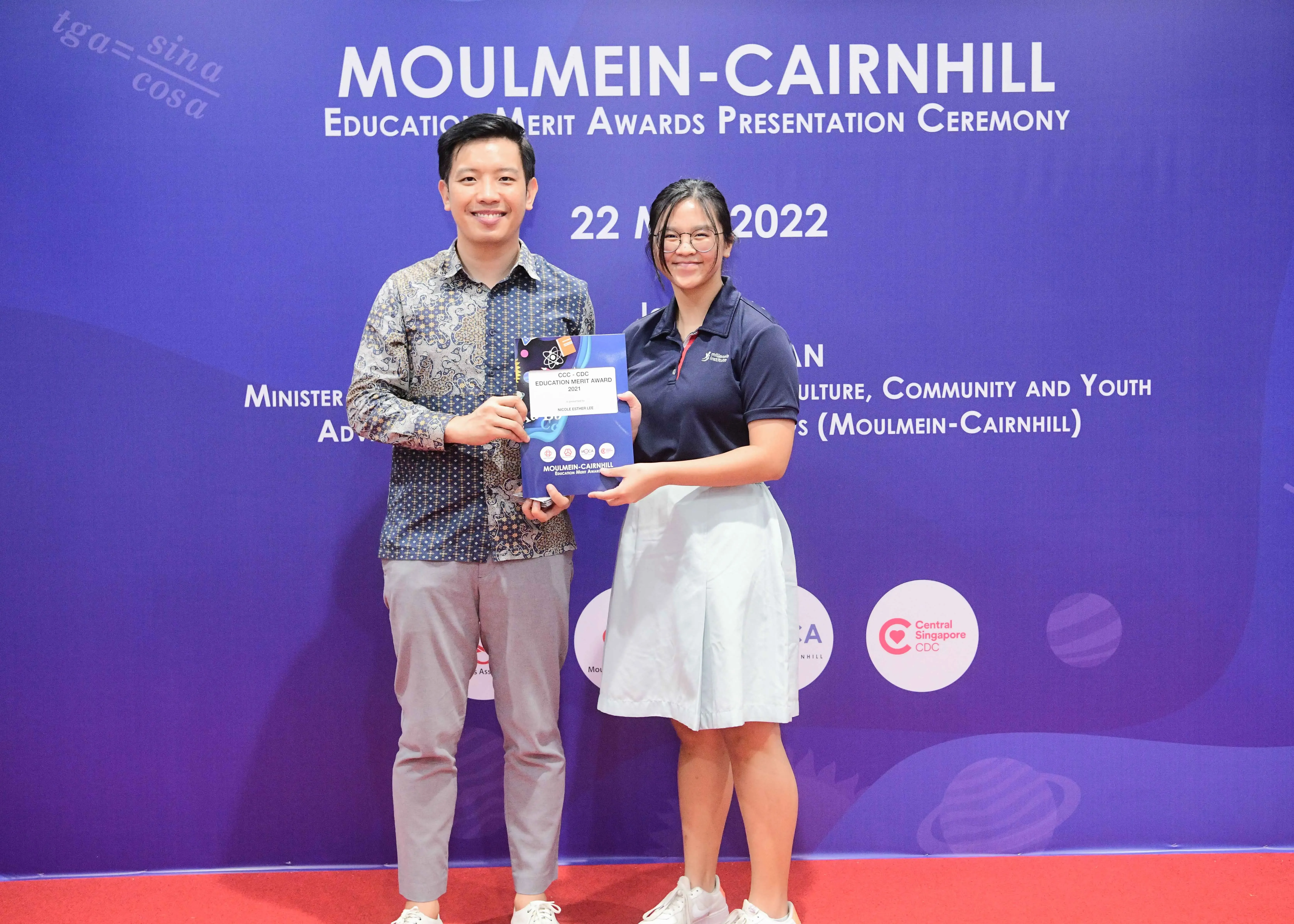 Two people smile while holding an award booklet at the Moulmein-Cairnhill Education Merit Awards Ceremony 2022.