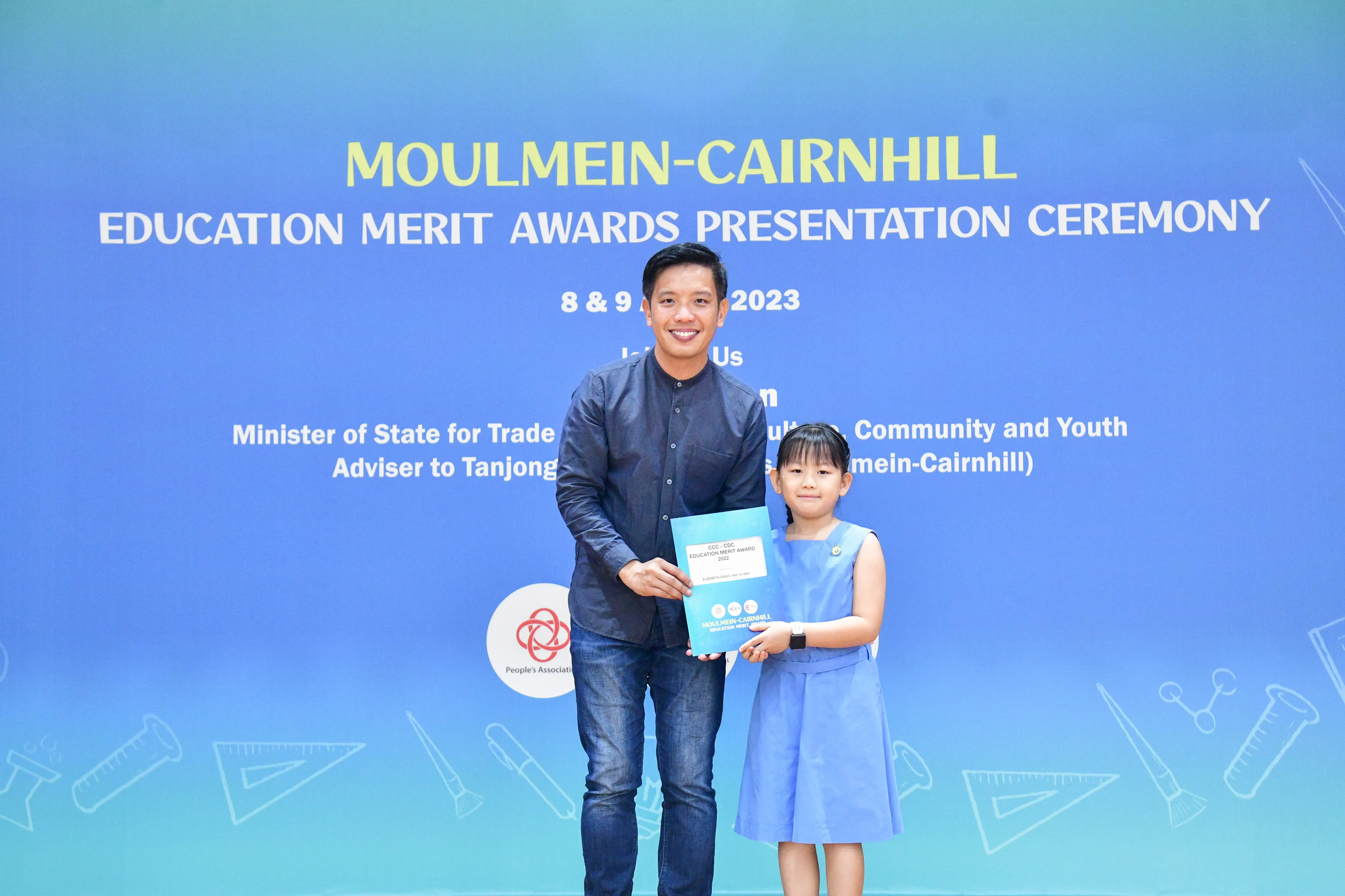A man and a young girl hold an award certificate together at the Moulmein-Cairnhill Education Merit Awards Ceremony 2023.
