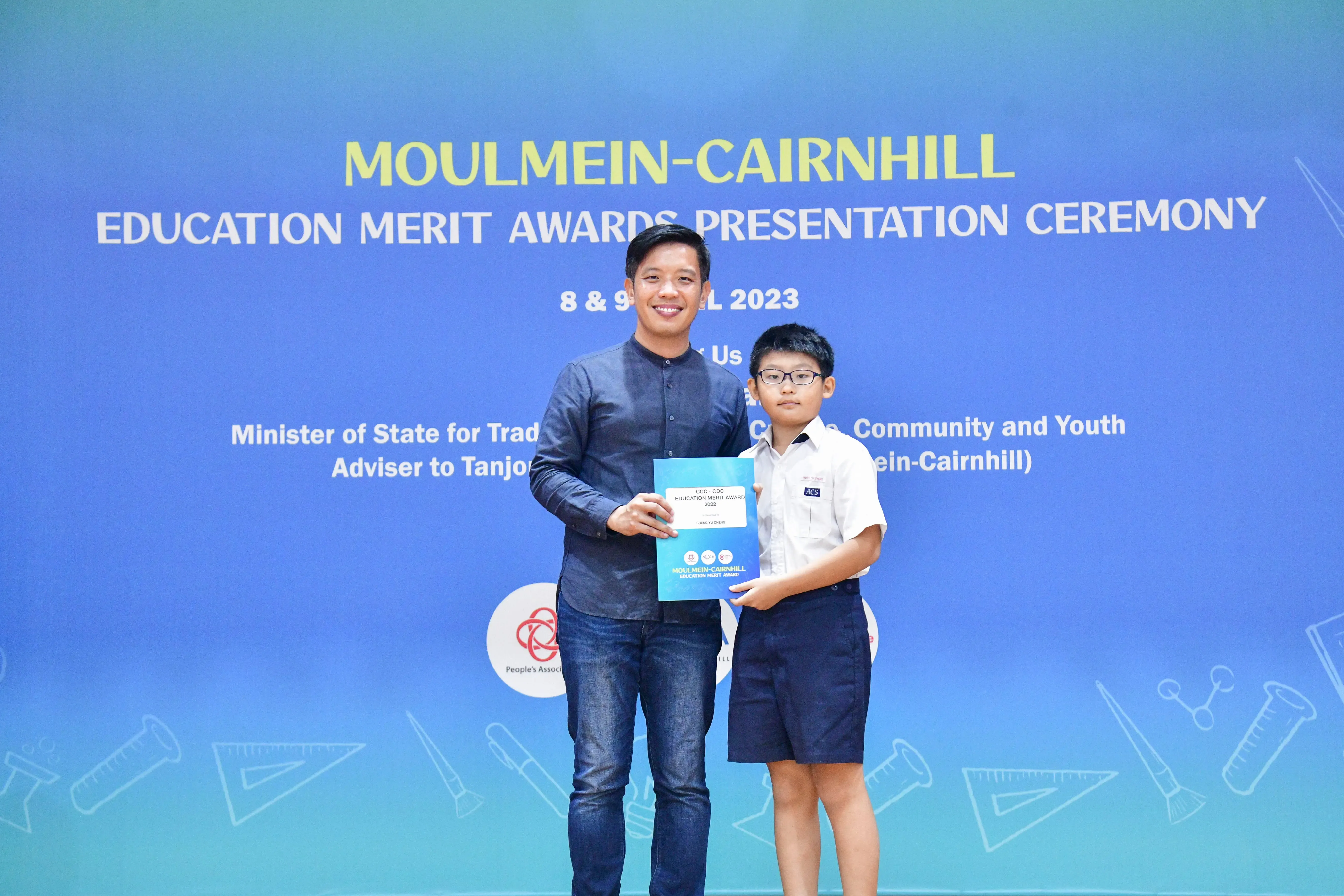 An adult and a young boy in school uniform hold a certificate at the Moulmein-Cairnhill Education Merit Awards 2023.