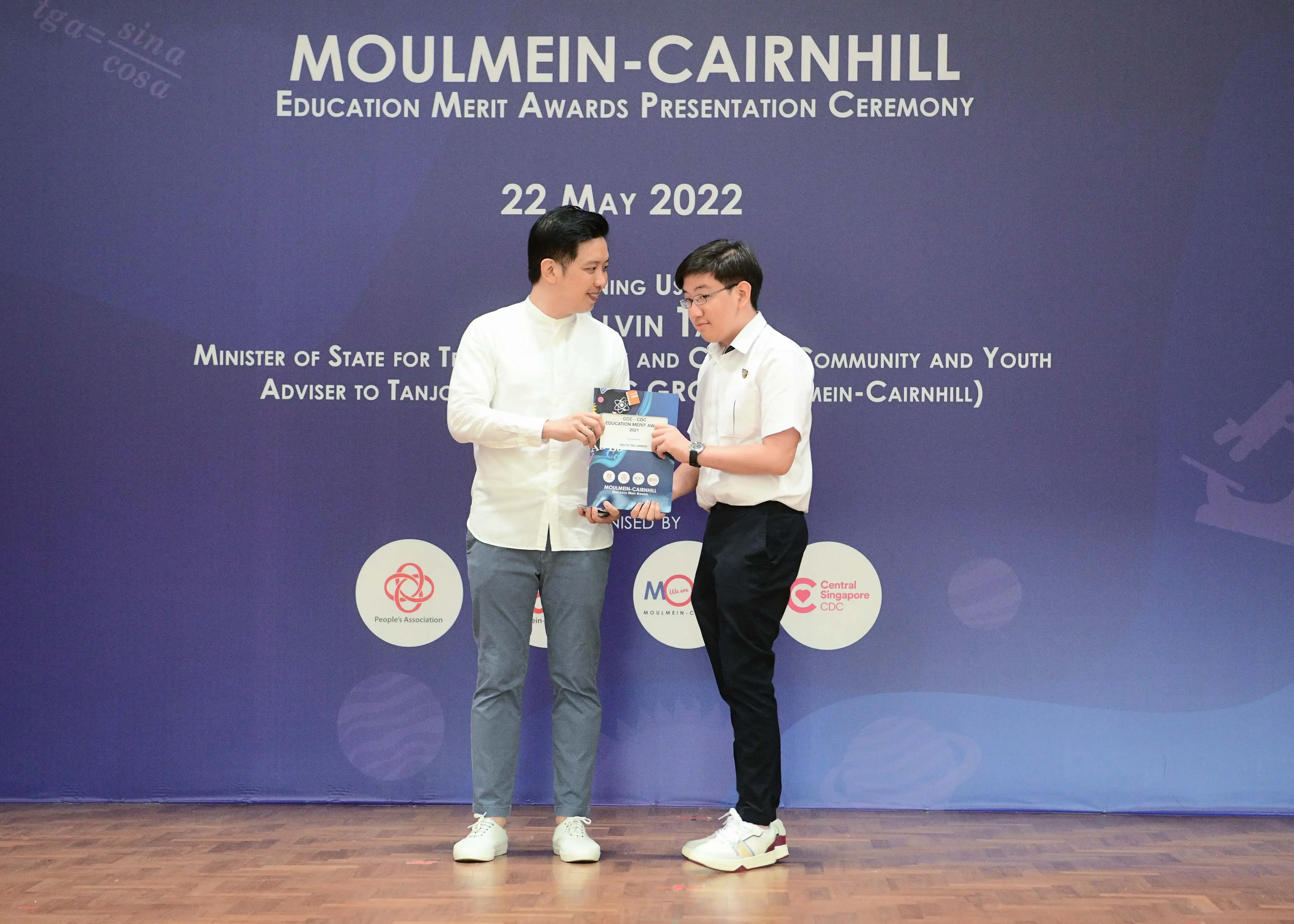 Two men exchange an award booklet on stage at the Moulmein-Cairnhill Education Merit Awards on 22 May 2022.