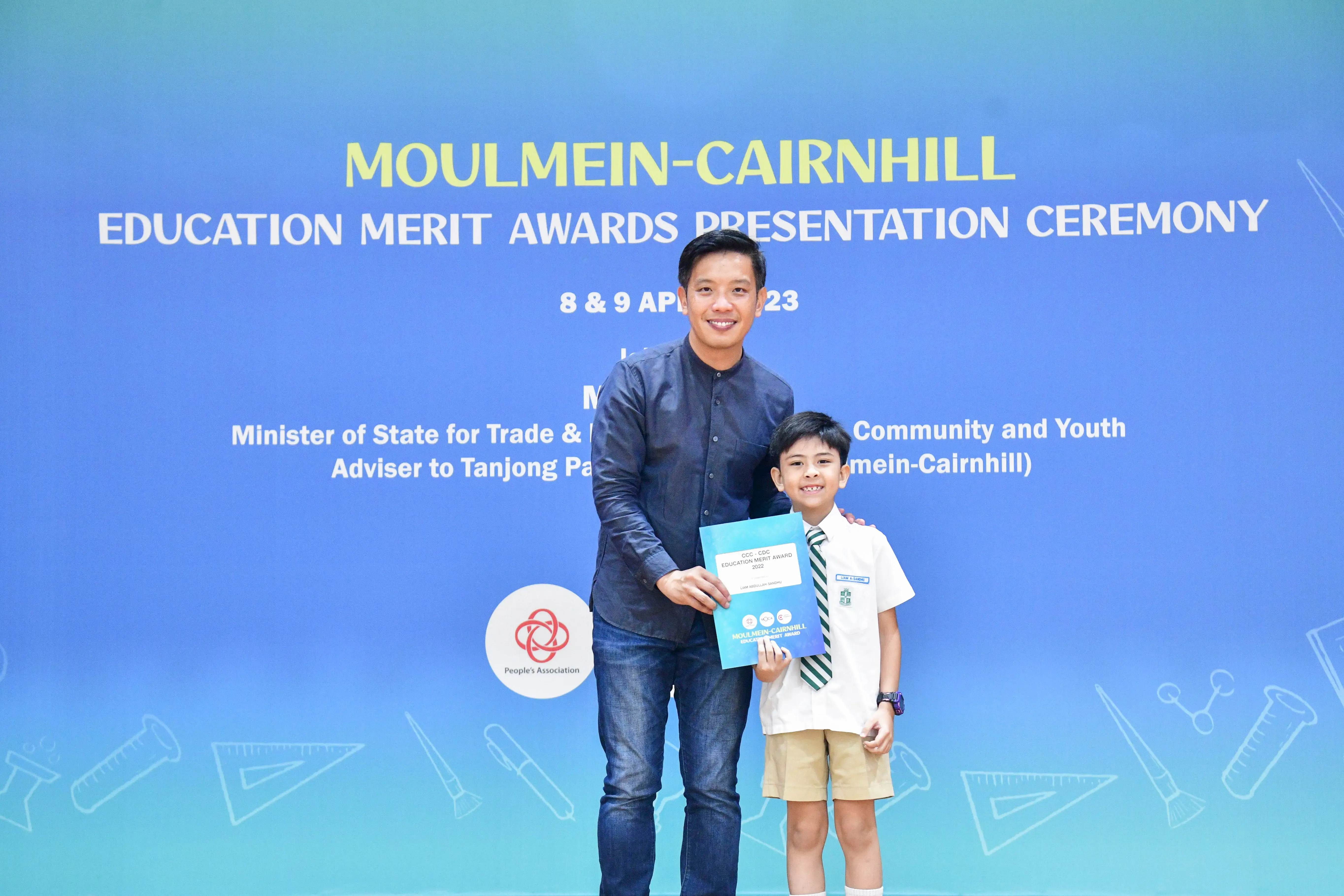 Man and young boy in school uniform hold a certificate at Moulmein-Cairnhill Education Merit Awards ceremony.