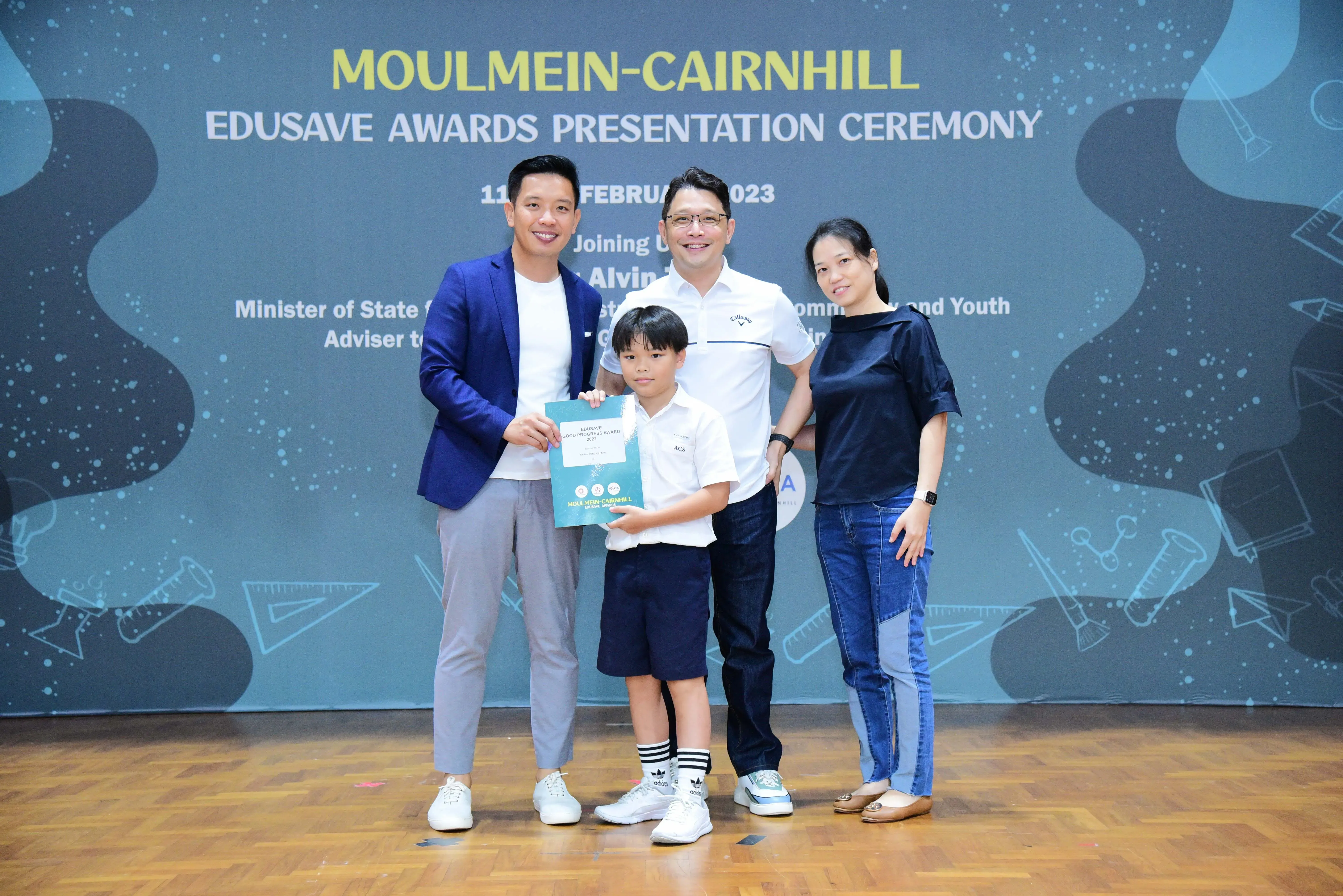 A young boy holds a certificate with three adults at the Moulmein-Cairnhill Edusave Awards Presentation Ceremony 2023.