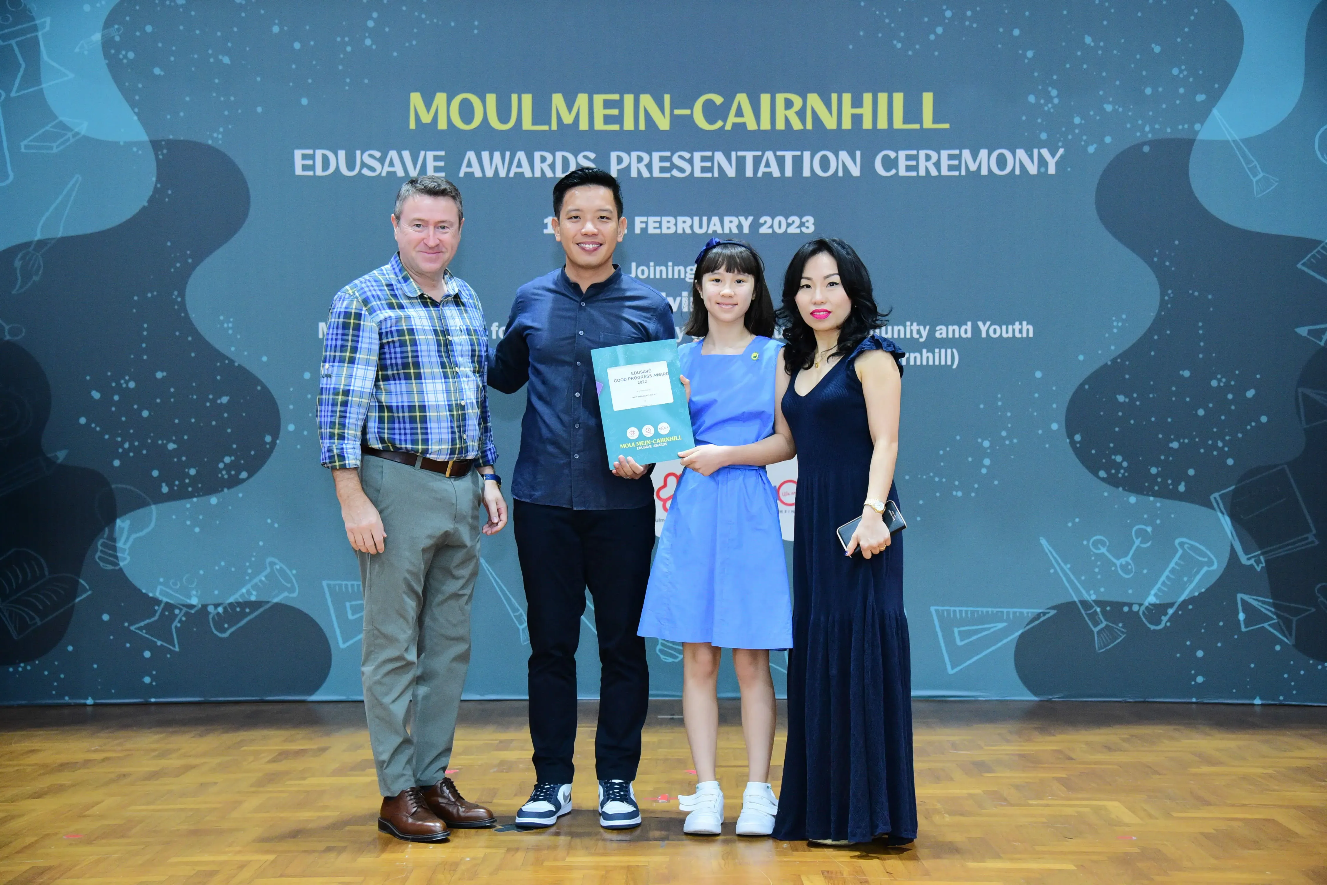 Four people pose at the Moulmein-Cairnhill Edusave Awards Presentation Ceremony in February 2023, with a girl holding a certificate.