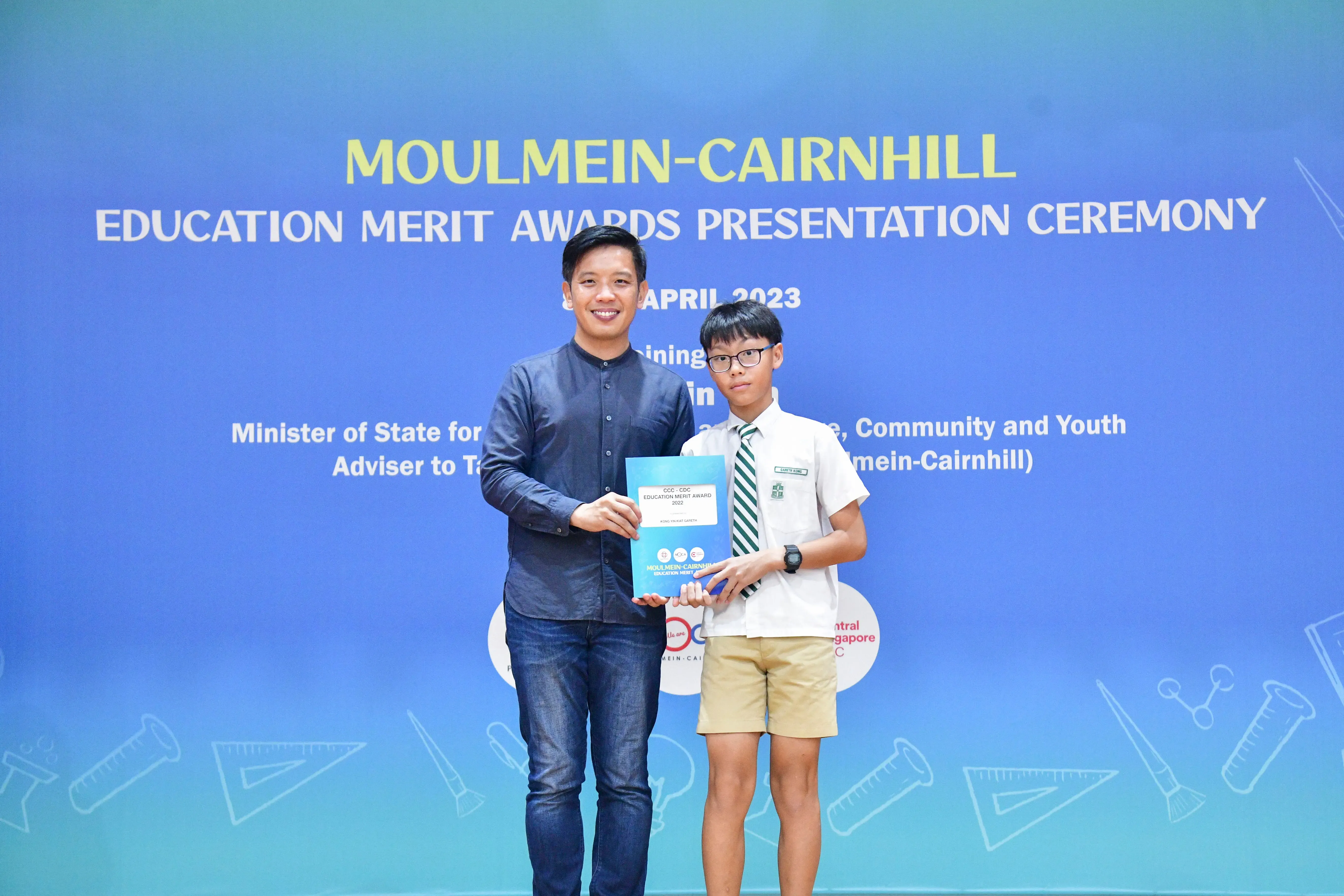 An adult and a young student hold a certificate at the Moulmein-Cairnhill Education Merit Awards Ceremony, April 2023.