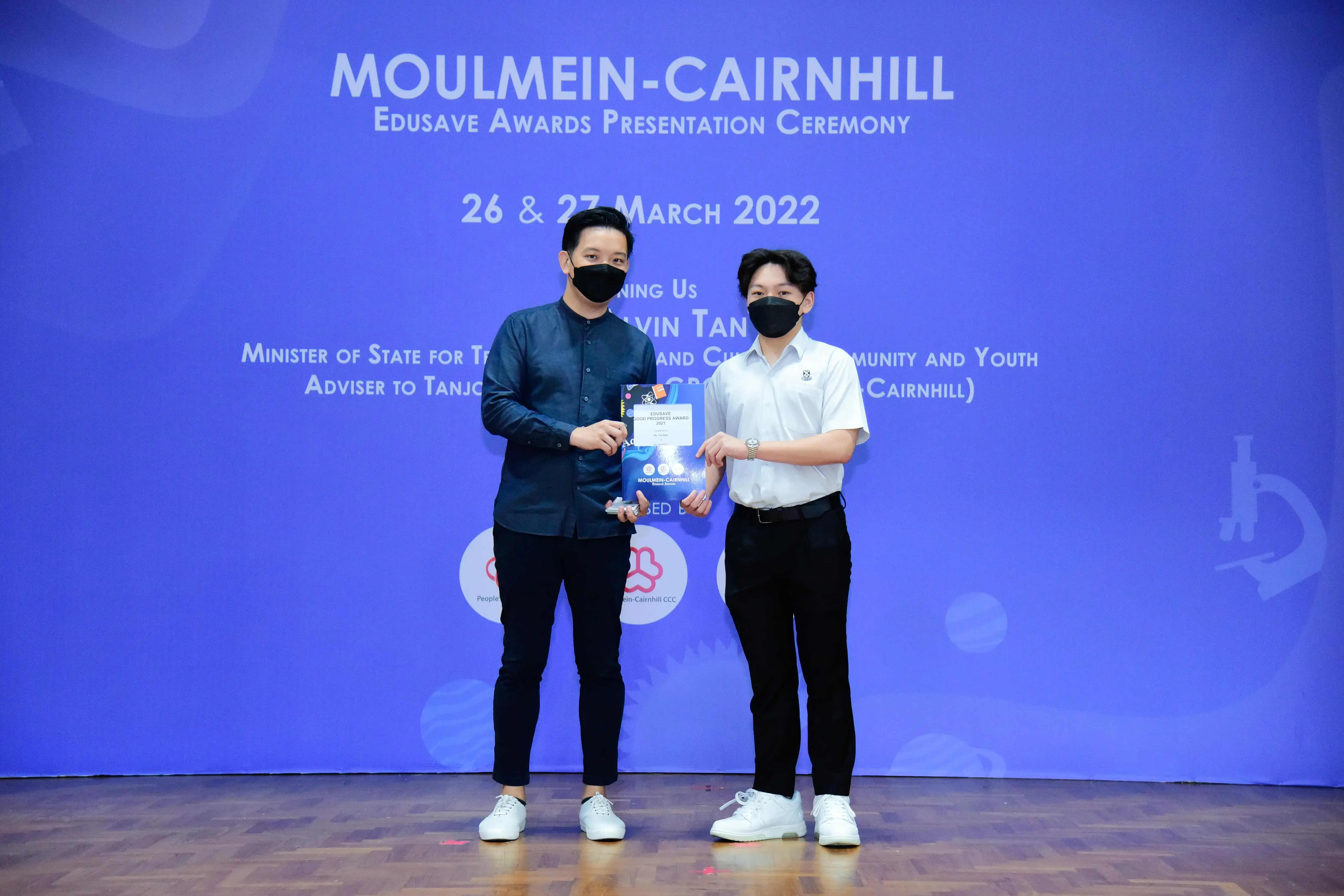 Two masked men hold a certificate at the Moulmein-Cairnhill Edusave Awards Presentation Ceremony, March 2022.