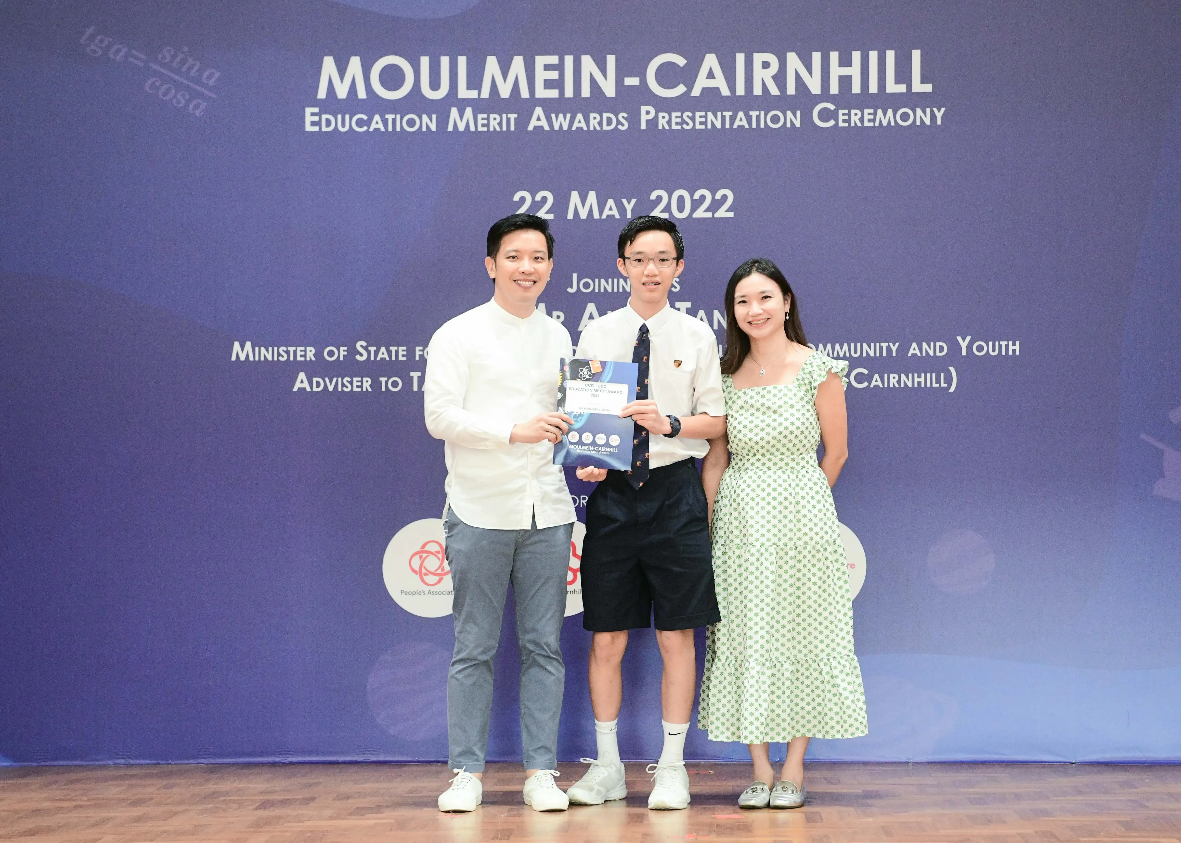 Three people pose holding an award booklet at the Moulmein-Cairnhill Education Merit Awards ceremony on 22 May 2022.