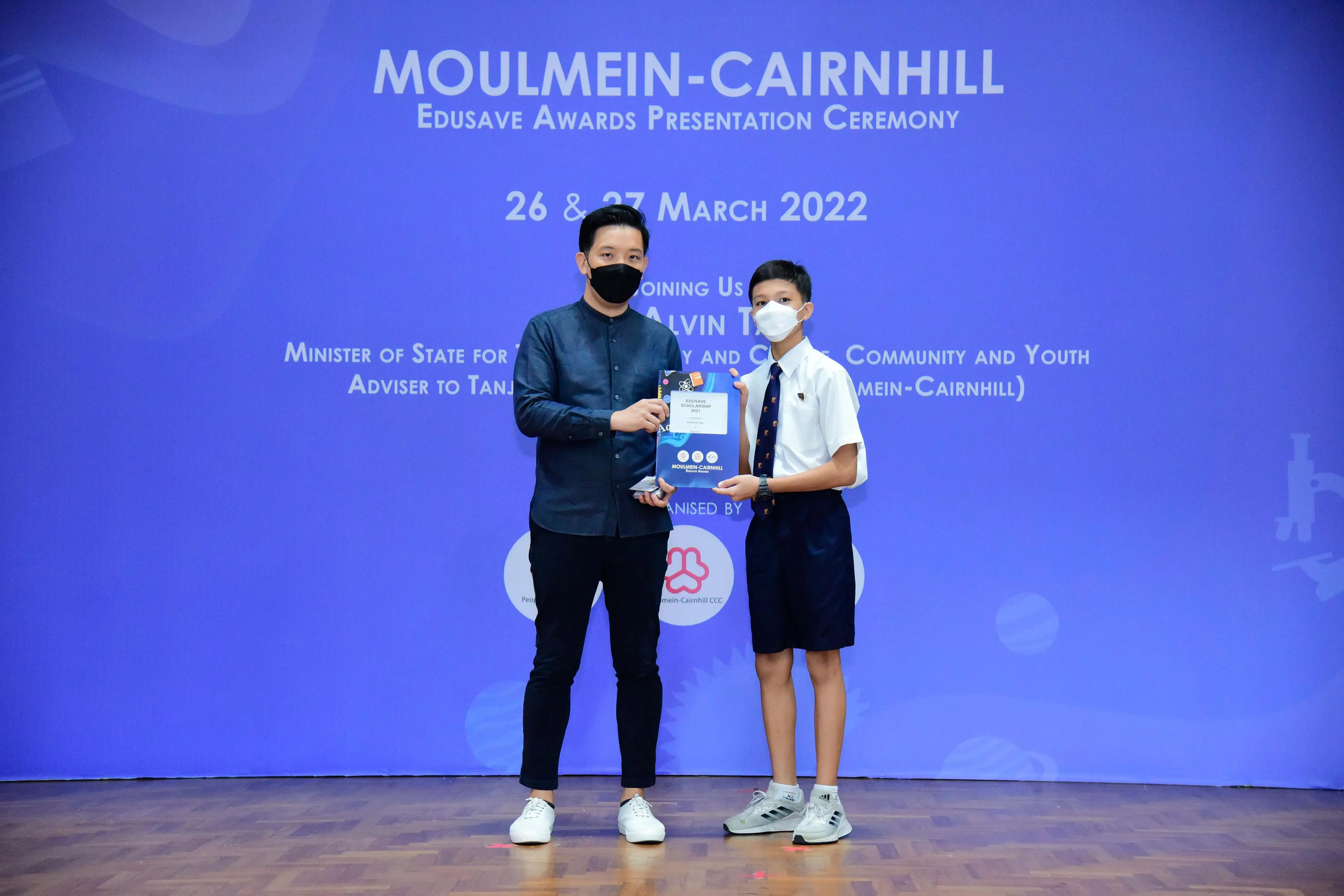 An adult and a young student in school uniform hold an award at the Moulmein-Cairnhill Edusave Awards Ceremony 2022.