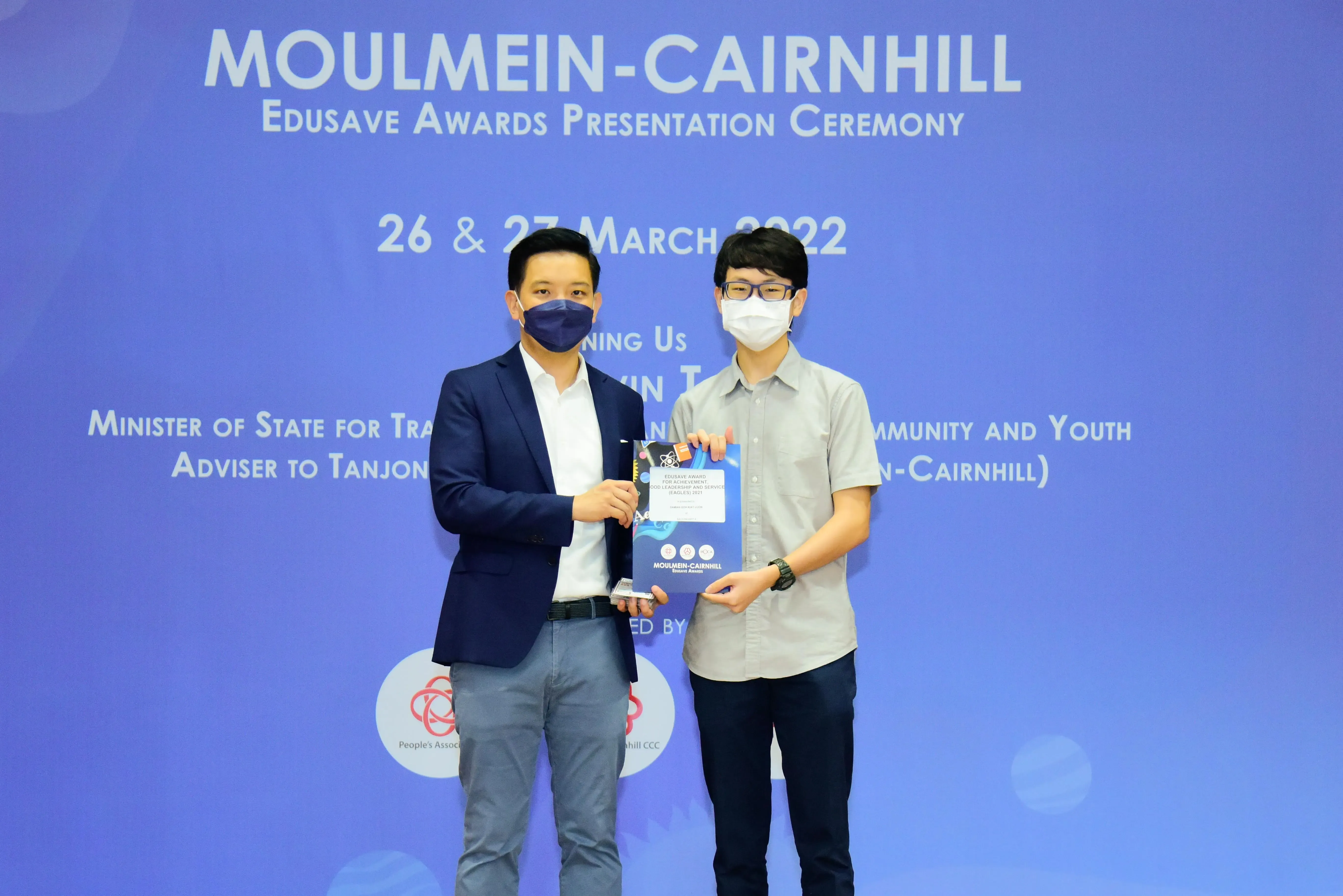 Two masked men hold an award certificate at the Moulmein-Cairnhill Edusave Awards Presentation Ceremony, March 2022.