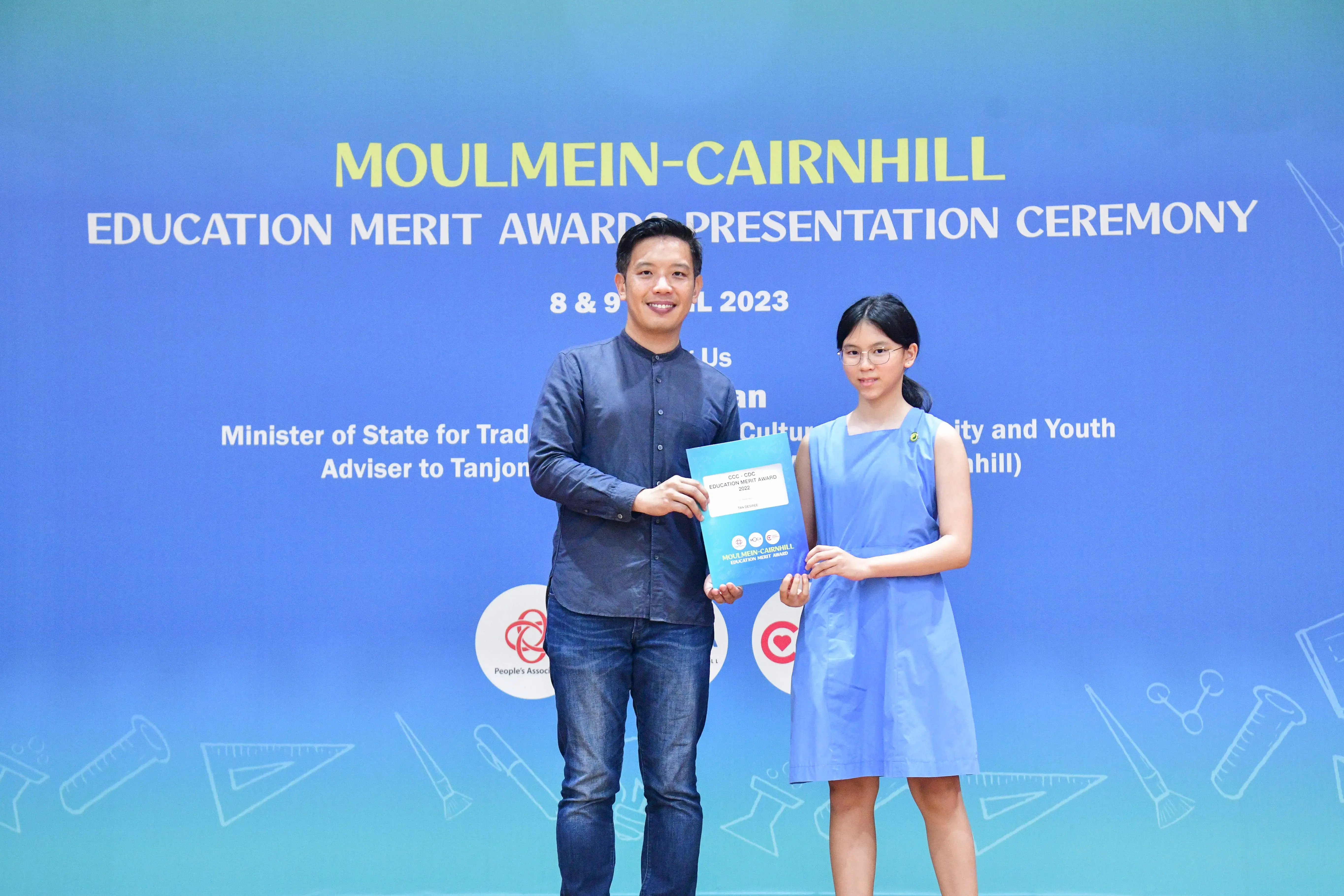 A man and a young girl hold a certificate together at the Moulmein-Cairnhill Education Merit Awards Ceremony 2023.