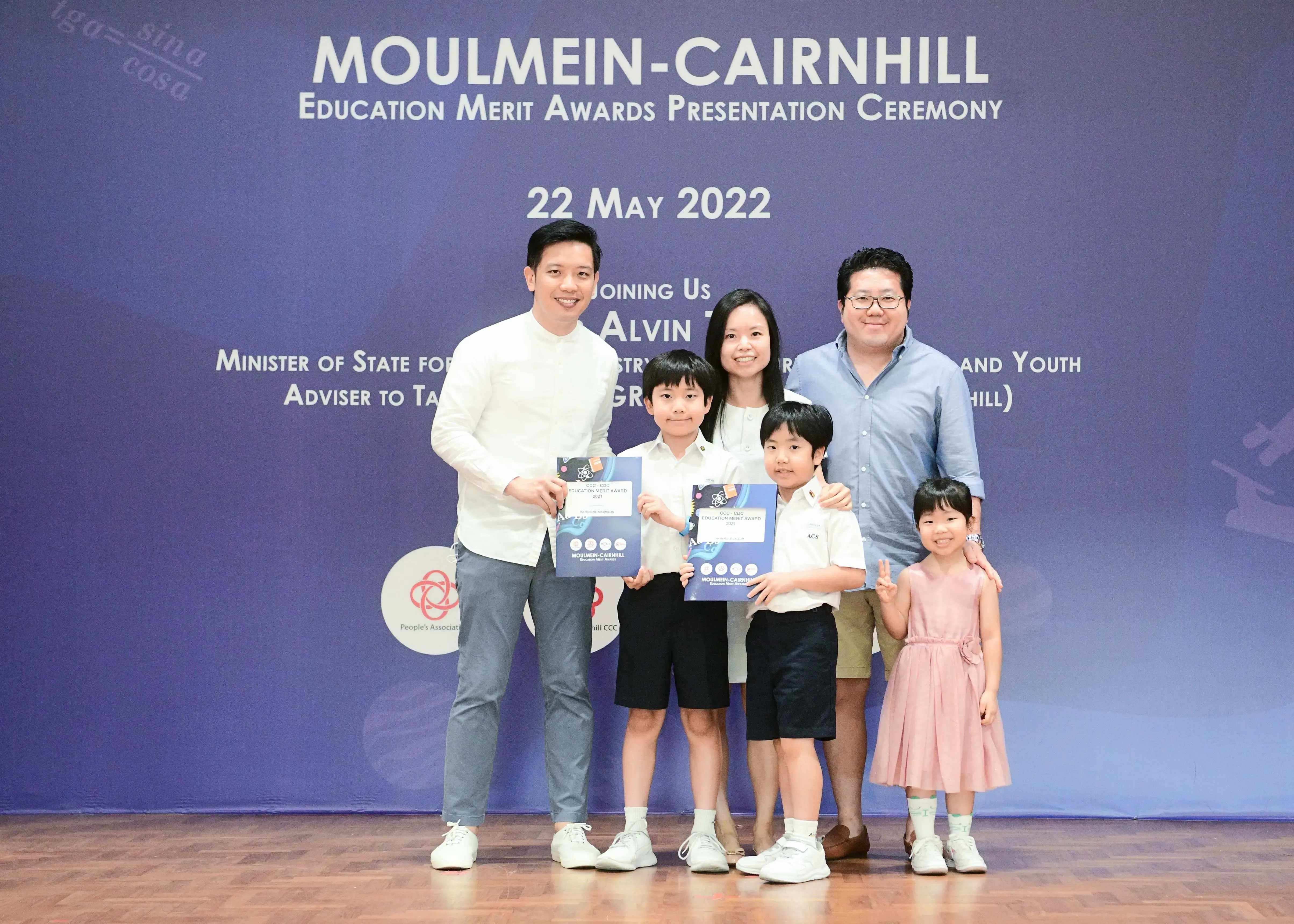 Five people pose at the Moulmein-Cairnhill Education Merit Awards ceremony on 22 May 2022, two boys holding award certificates.