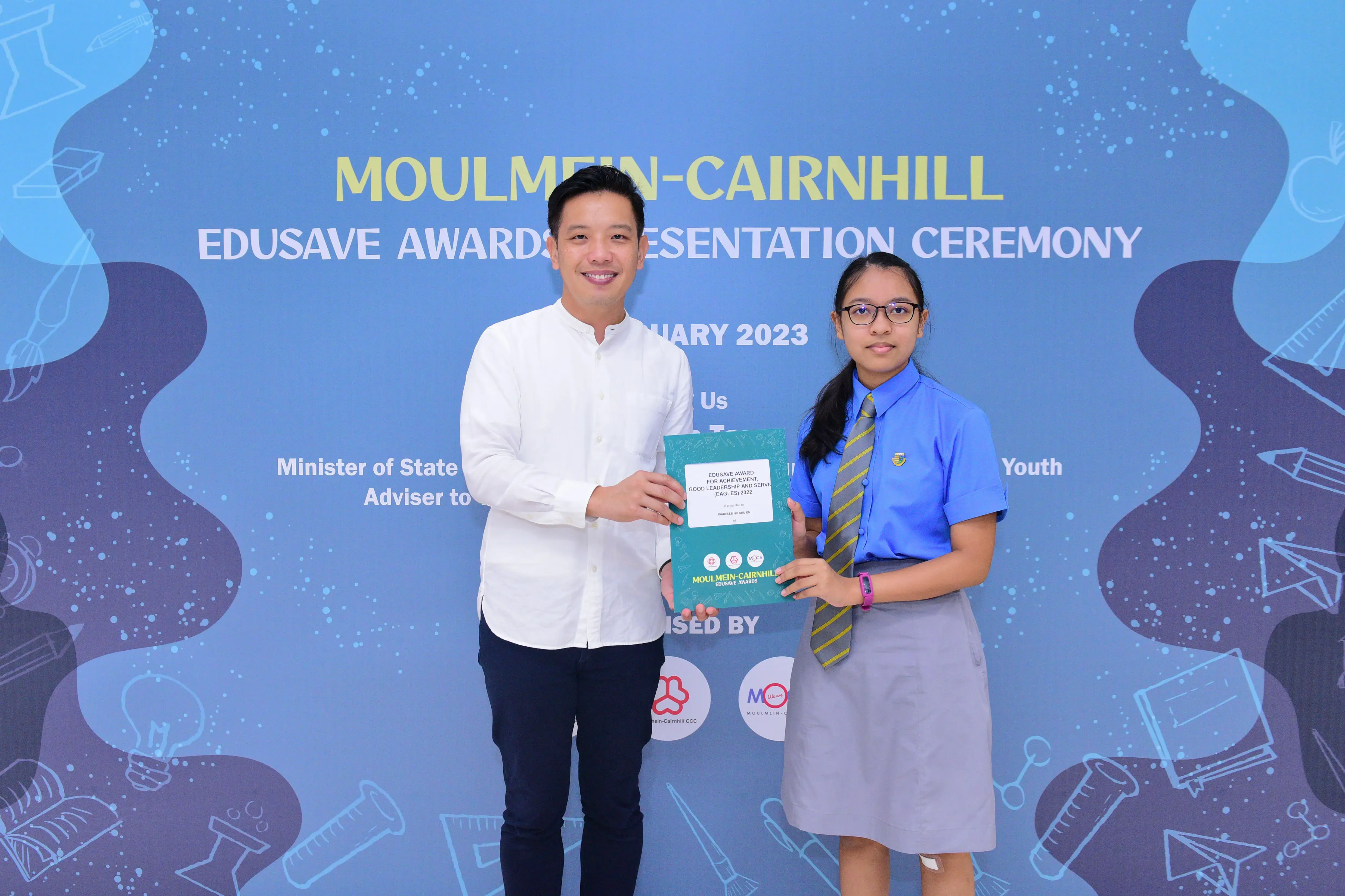 A man and a school girl hold a certificate together at the Moulmein-Cairnhill Edusave Awards Ceremony 2023.