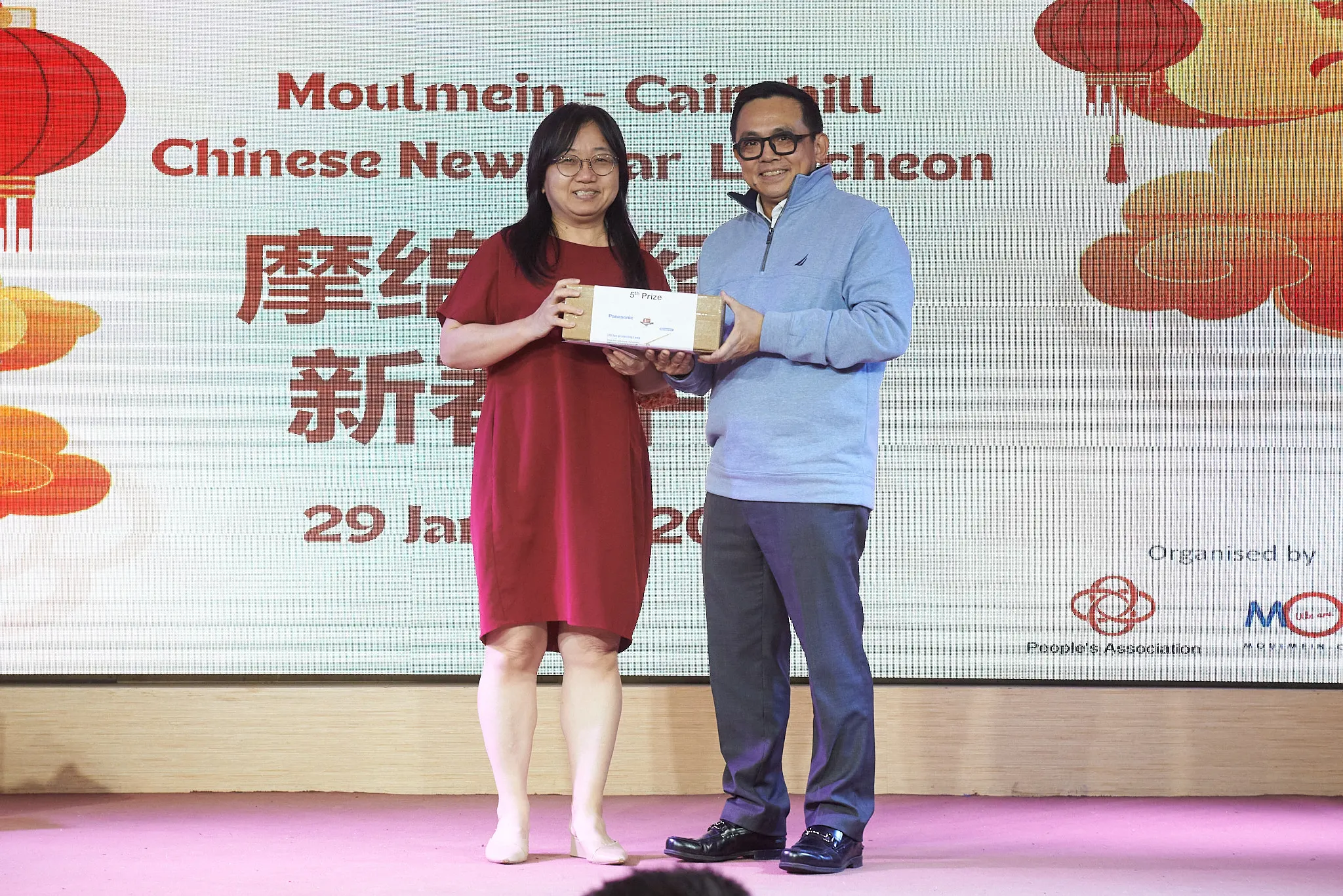 Two people hold a prize box on stage at the Moulmein-Cairnhill Chinese New Year Luncheon event.