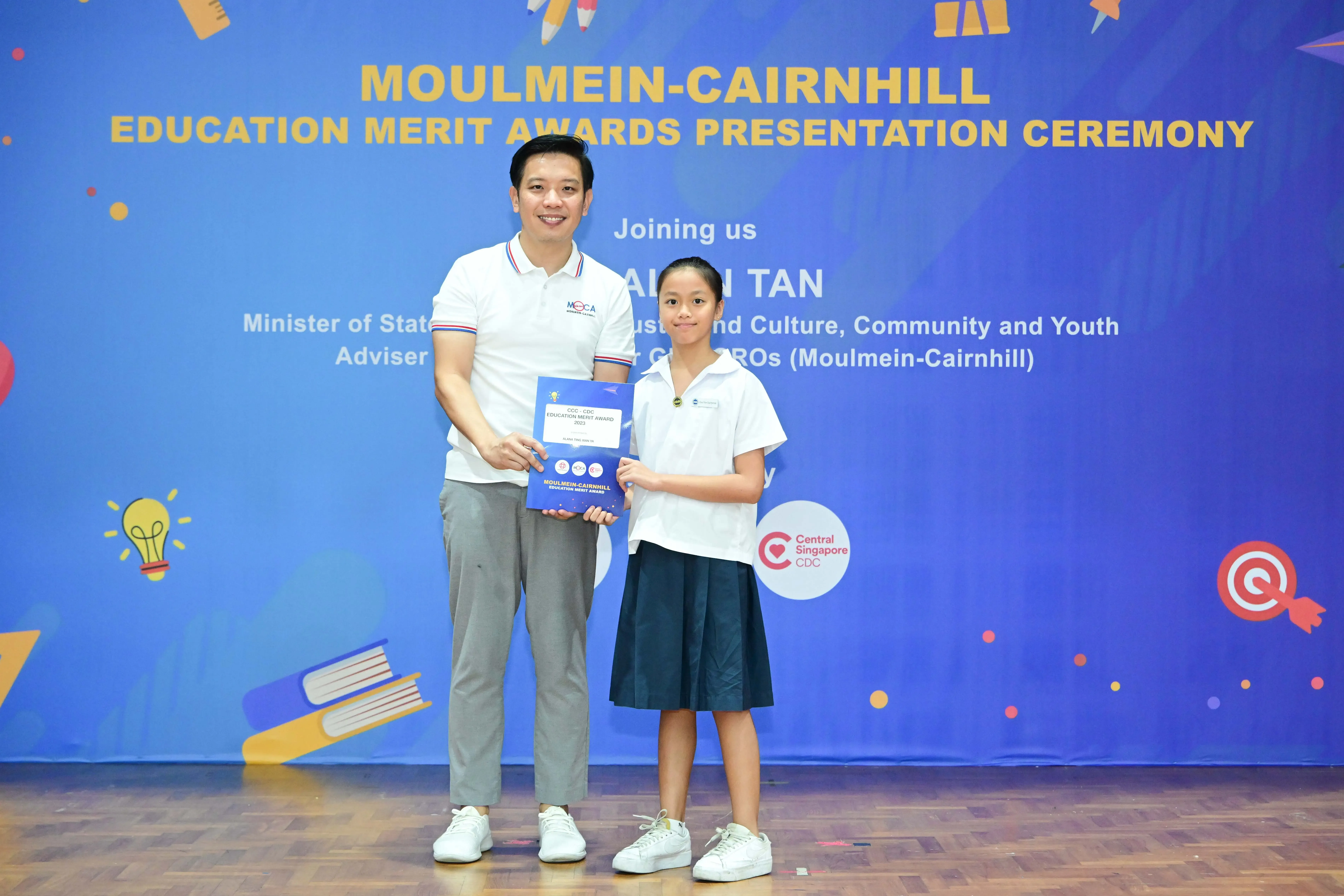 A man and a young girl hold an award certificate at the Moulmein-Cairnhill Education Merit Awards Presentation Ceremony.