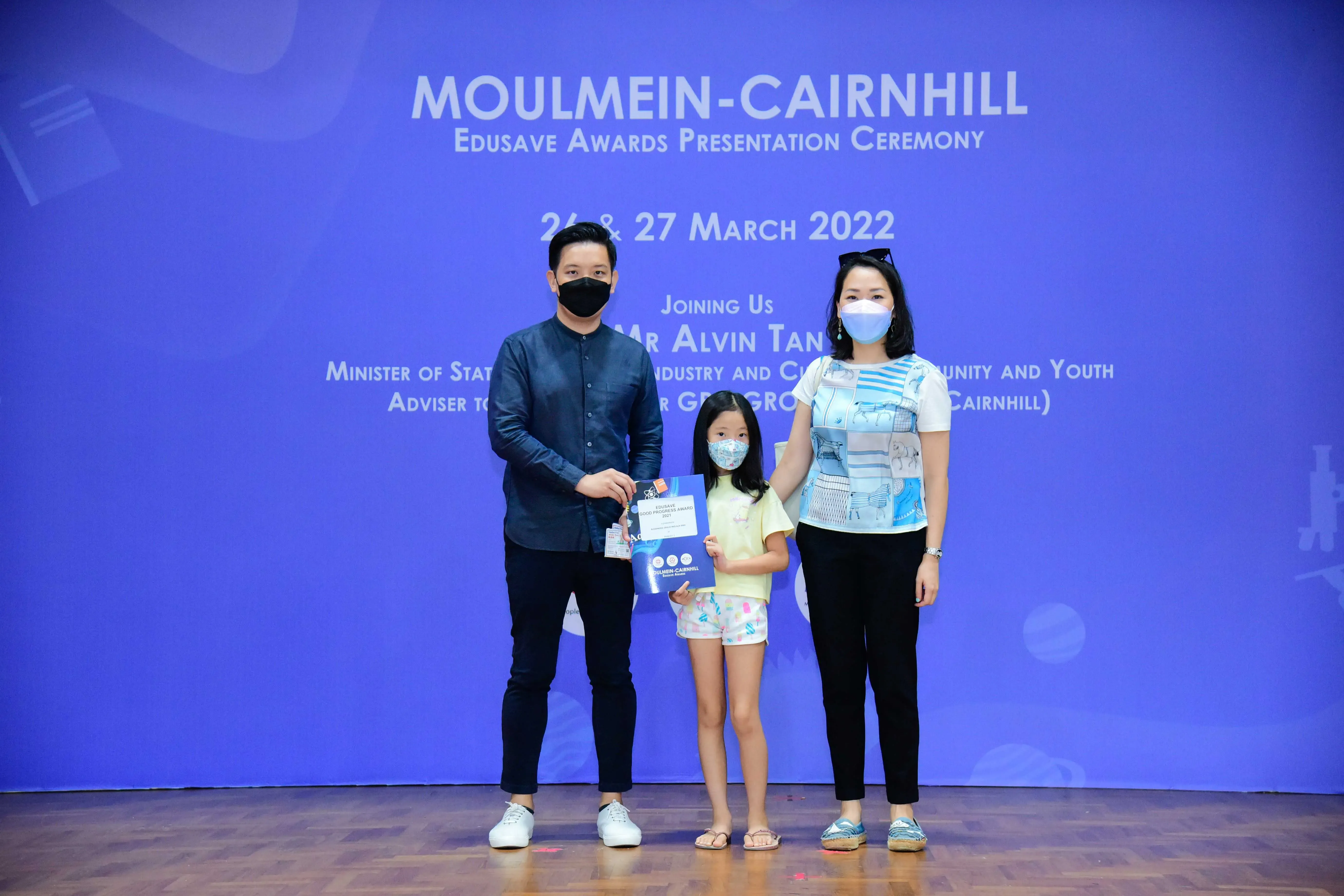Three masked people pose on a stage at the Moulmein-Cairnhill Edusave Awards Ceremony, March 2022.