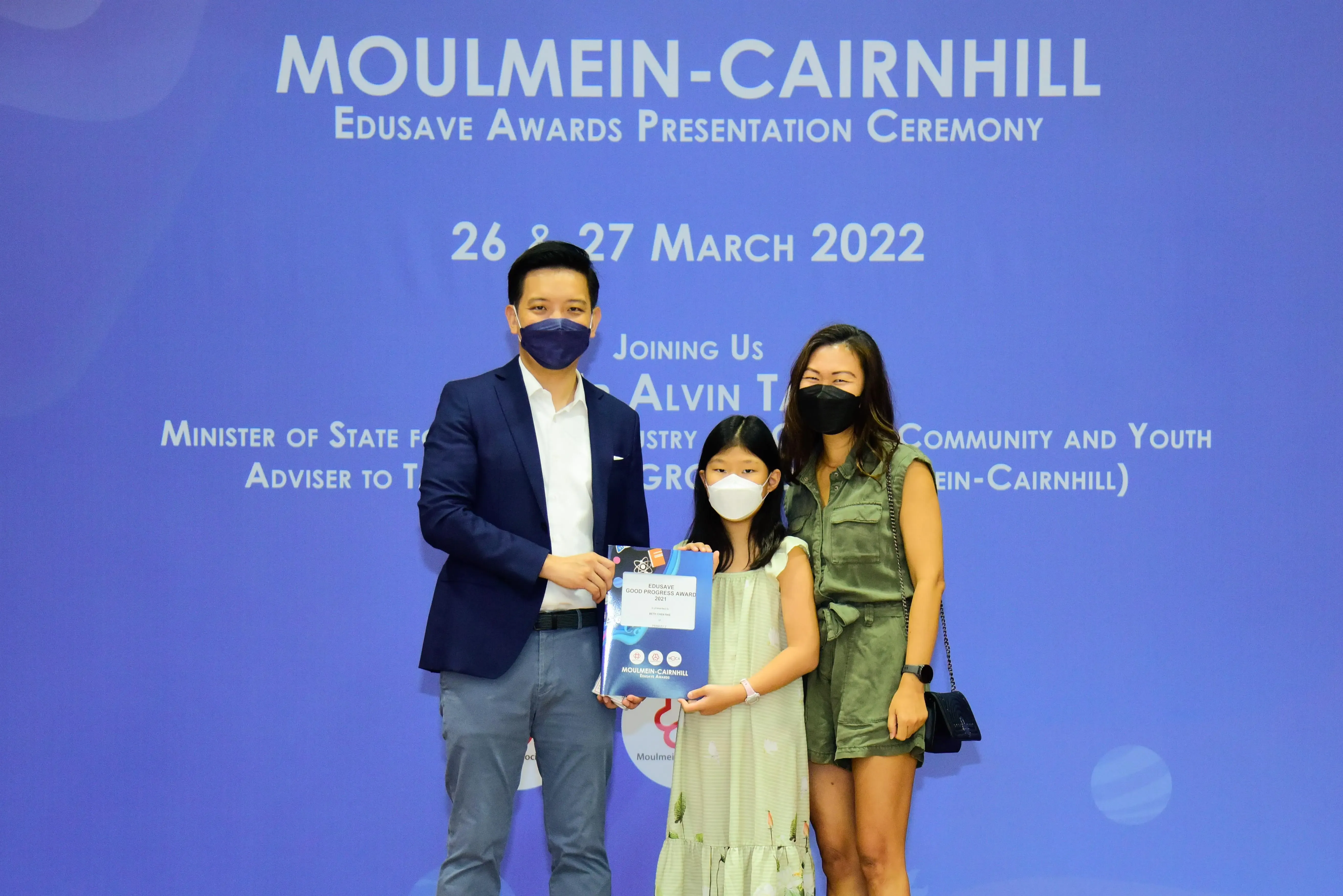 Three masked people pose at the Moulmein-Cairnhill Edusave Awards Ceremony on 26-27 March 2022, holding an award.