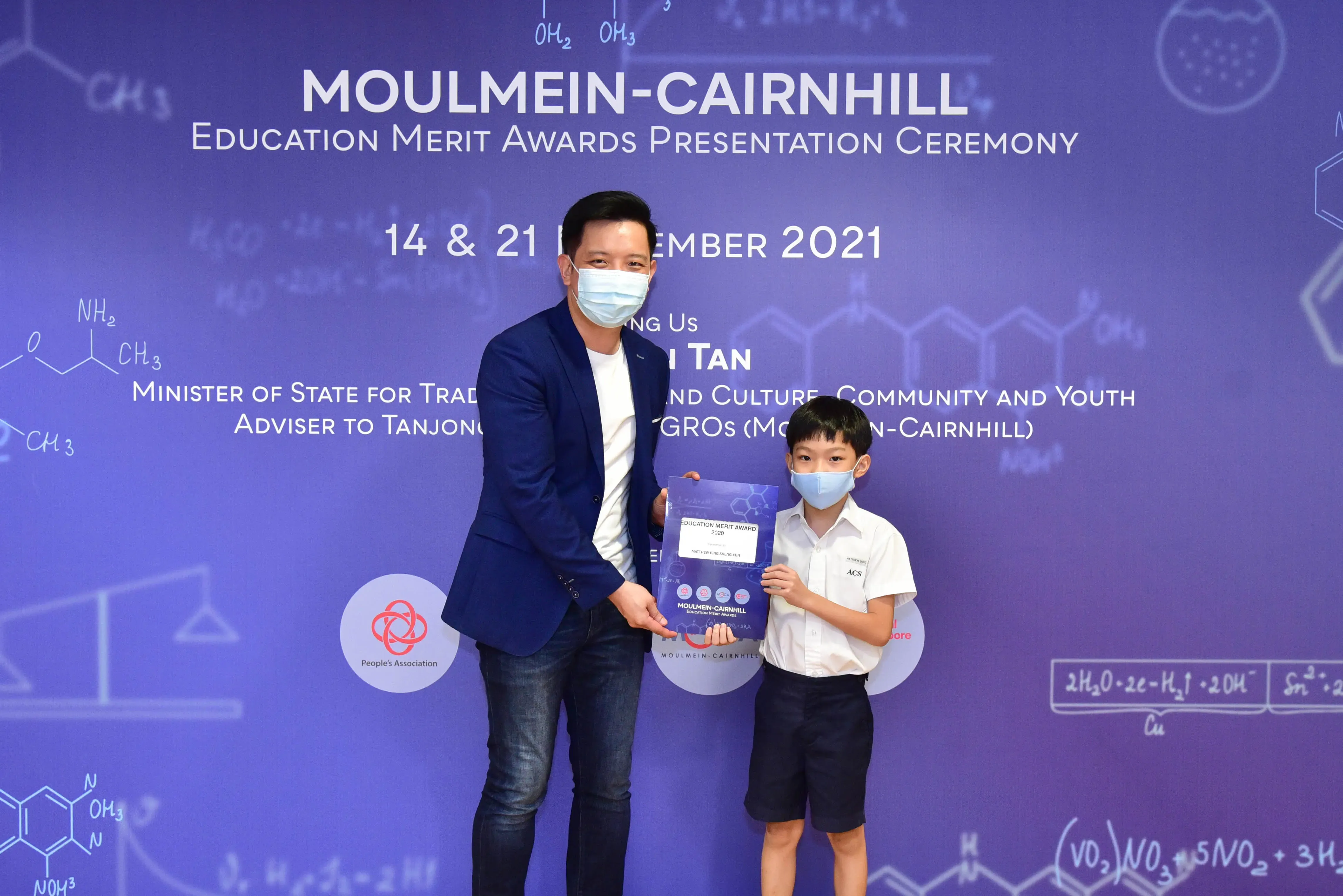 An adult and a young boy wearing masks hold an award certificate at the Moulmein-Cairnhill Education Merit Awards 2021.