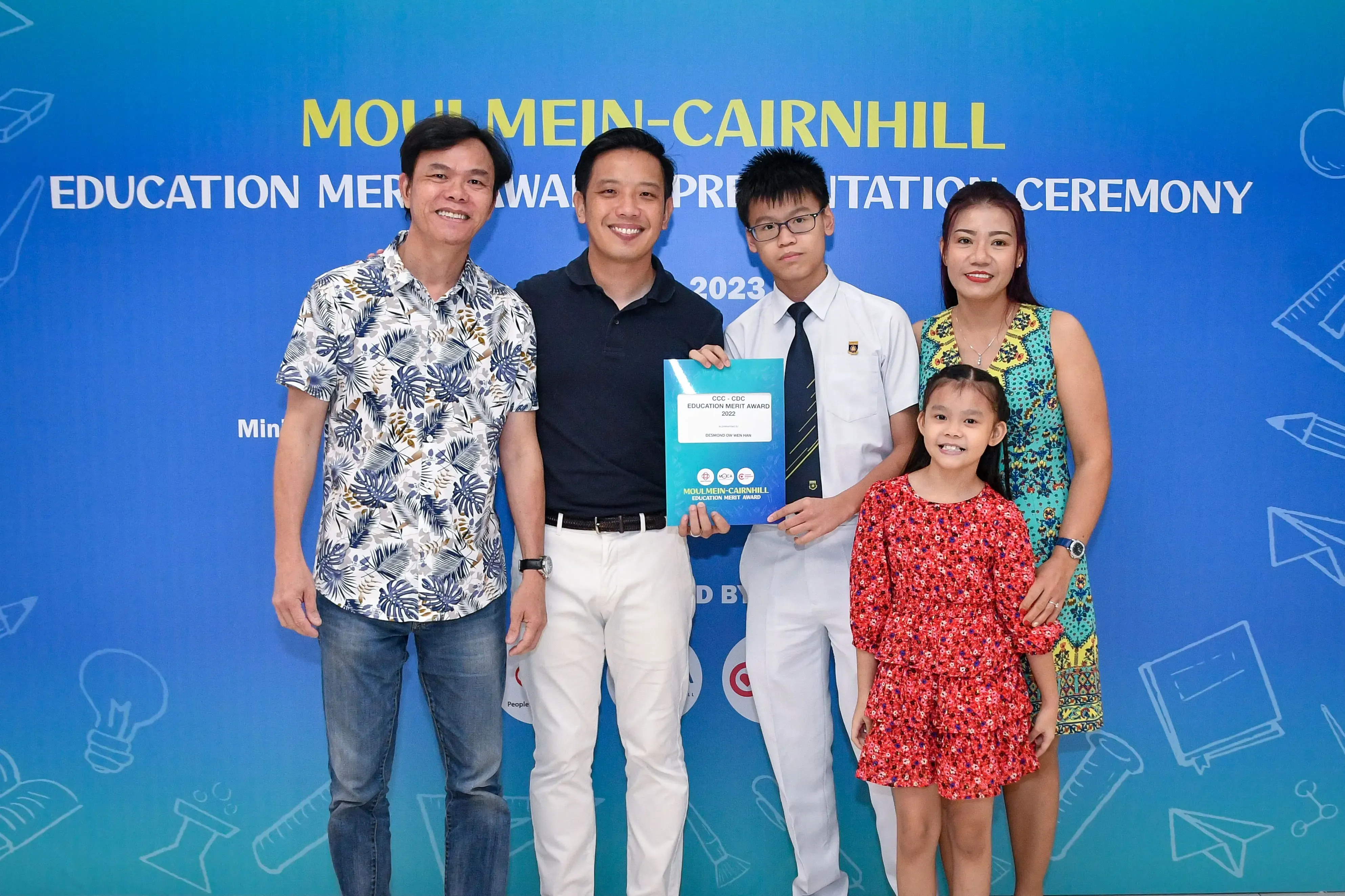 Four adults and a young girl pose at the Moulmein-Cairnhill Education Merit Award 2023 ceremony, holding an award certificate.