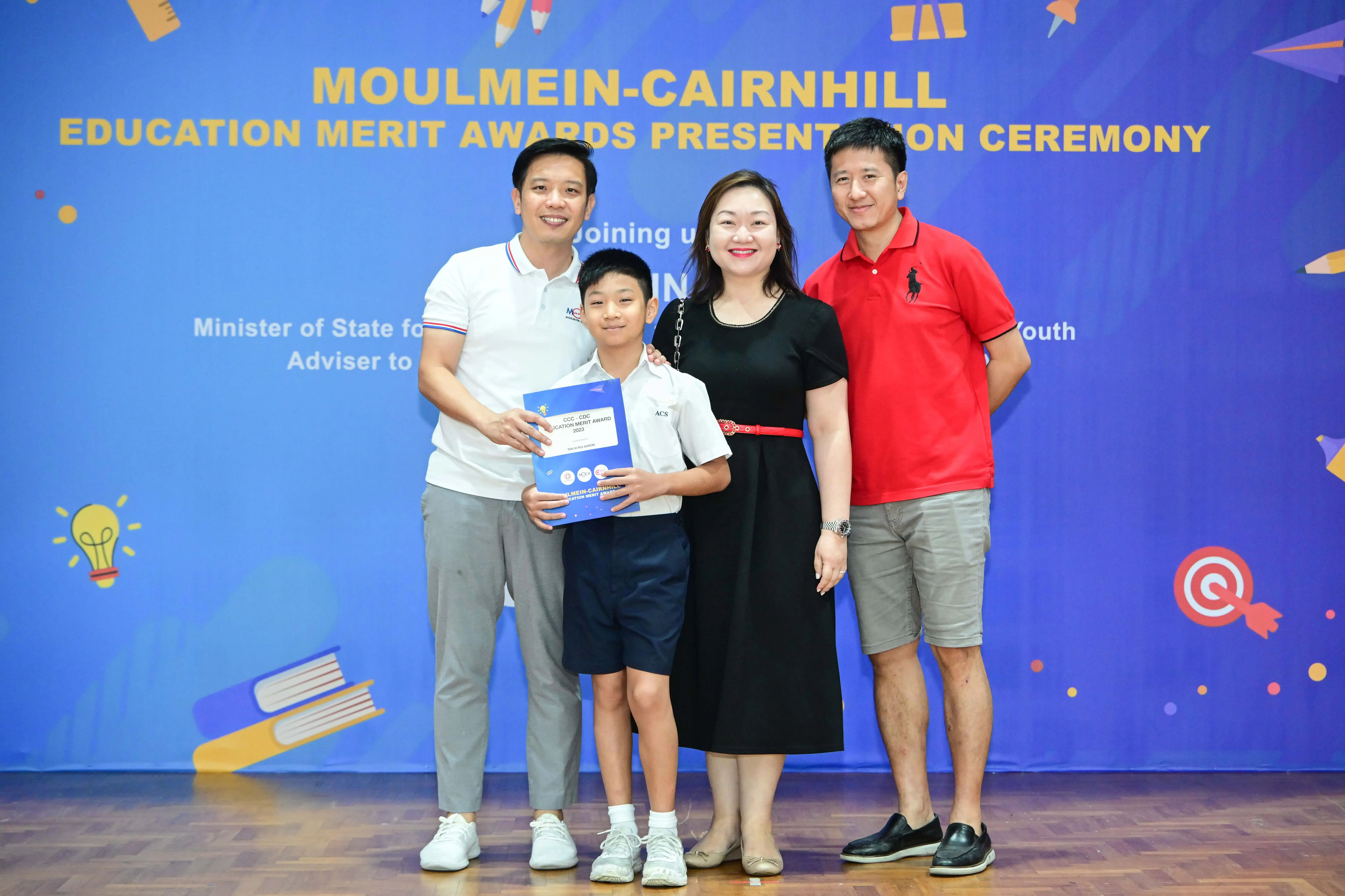 A boy holding an award certificate poses with three adults at the Moulmein-Cairnhill Education Merit Awards Ceremony.