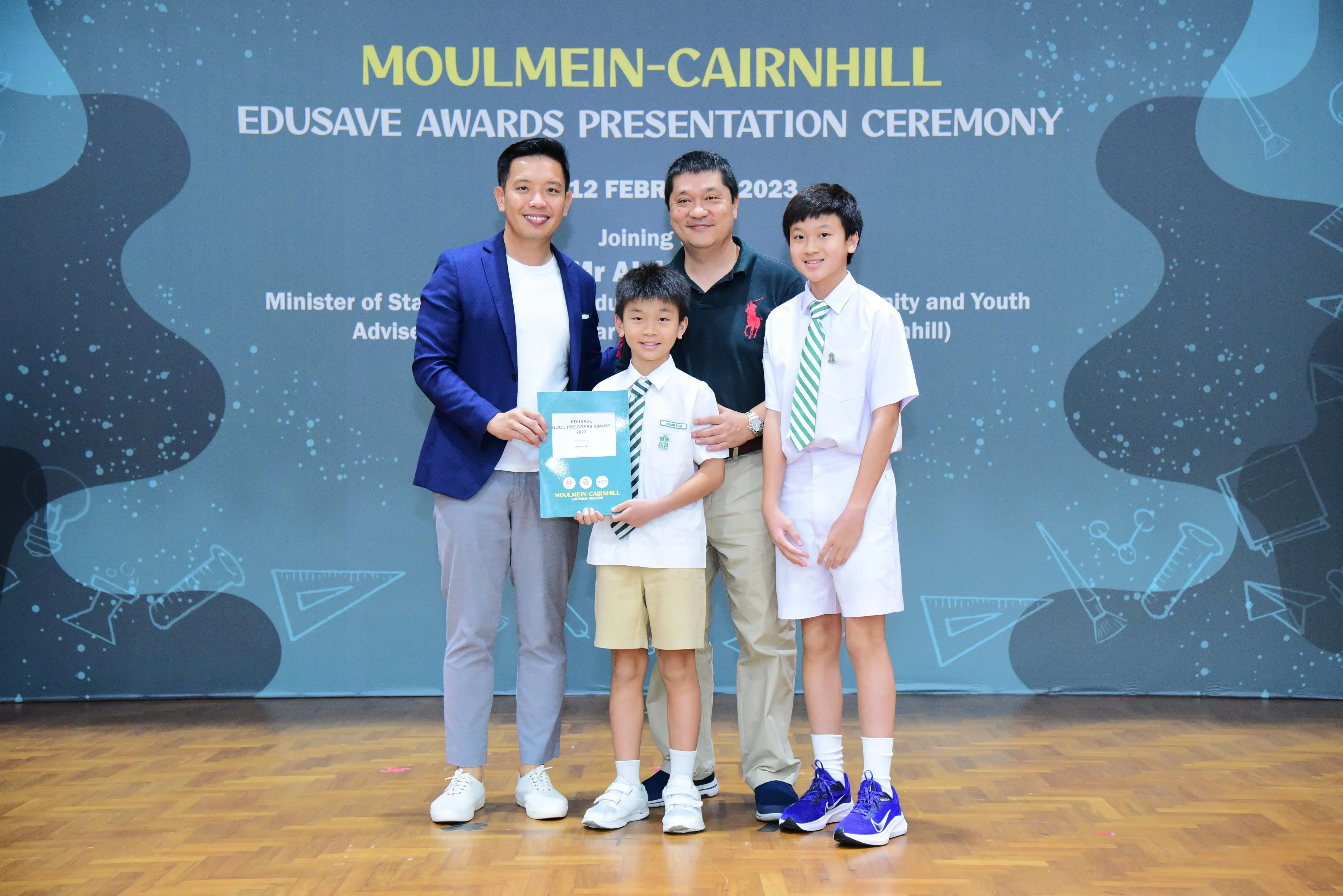 Two men and two boys in school uniforms pose at the Moulmein-Cairnhill Edusave Awards Presentation Ceremony 2023.