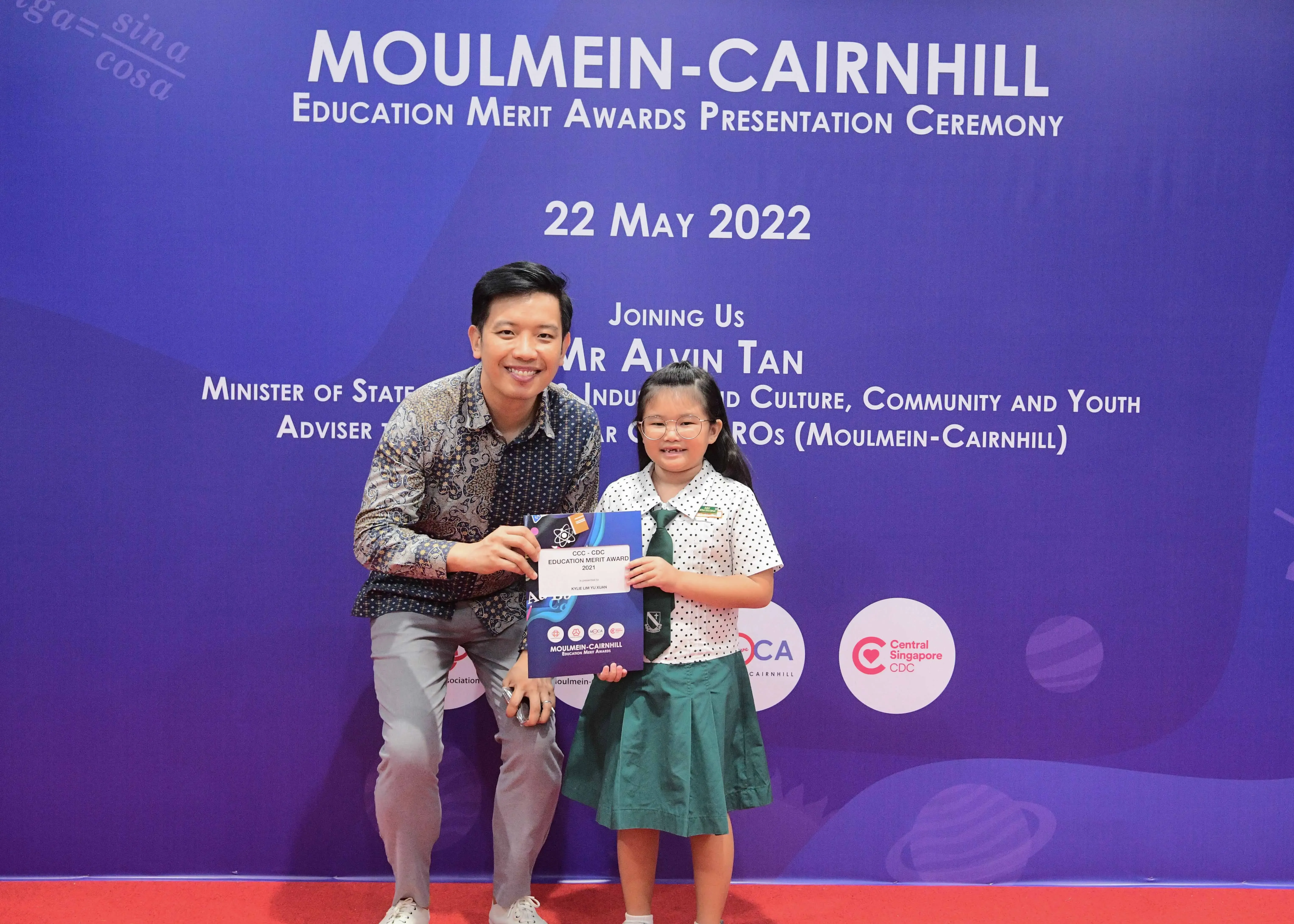 A man and a young girl in school uniform hold an award certificate at the Moulmein-Cairnhill Education Merit Awards ceremony on 22 May 2022.