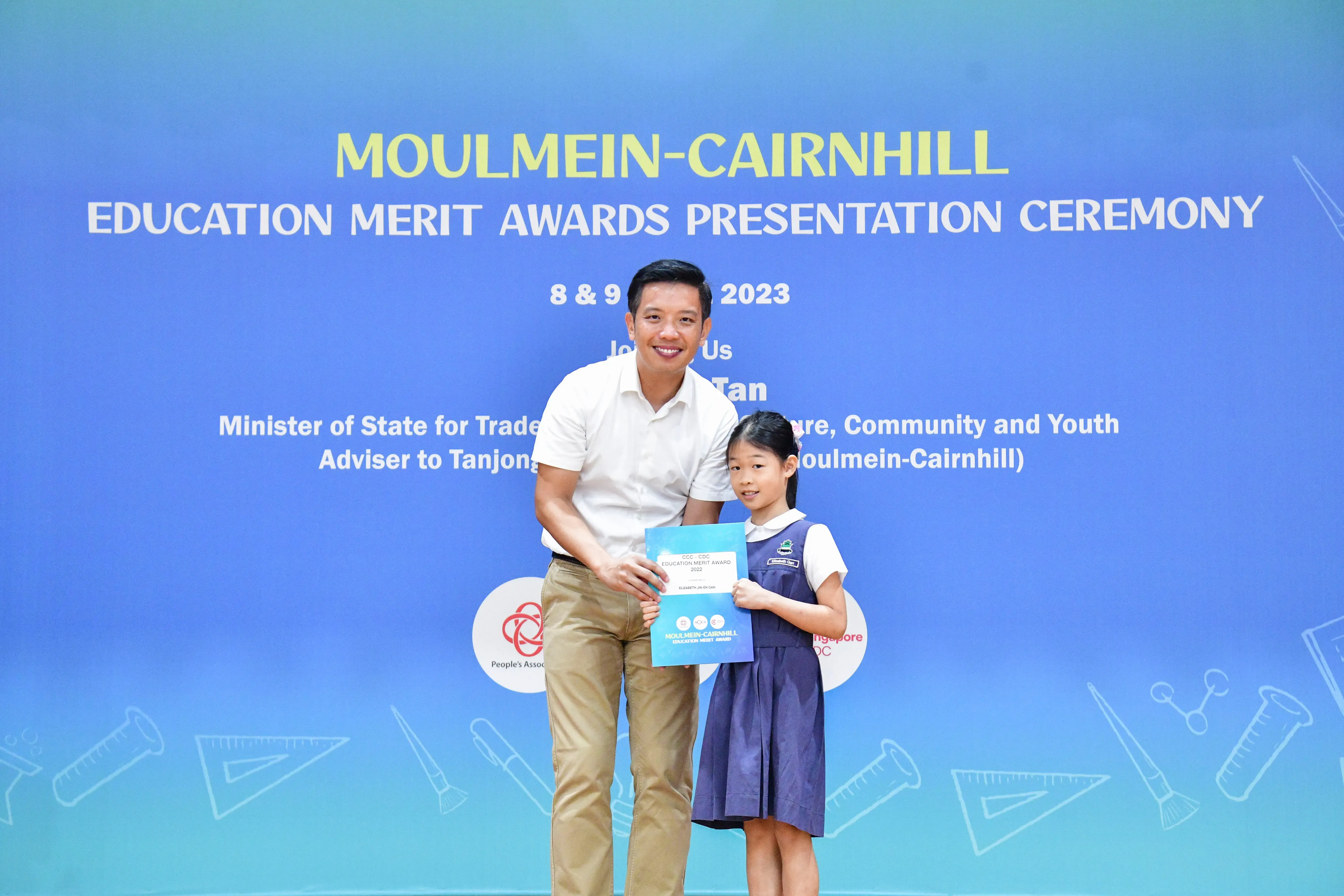 A man and a young girl in school uniform hold an award certificate at the Moulmein-Cairnhill Education Merit Awards 2023.
