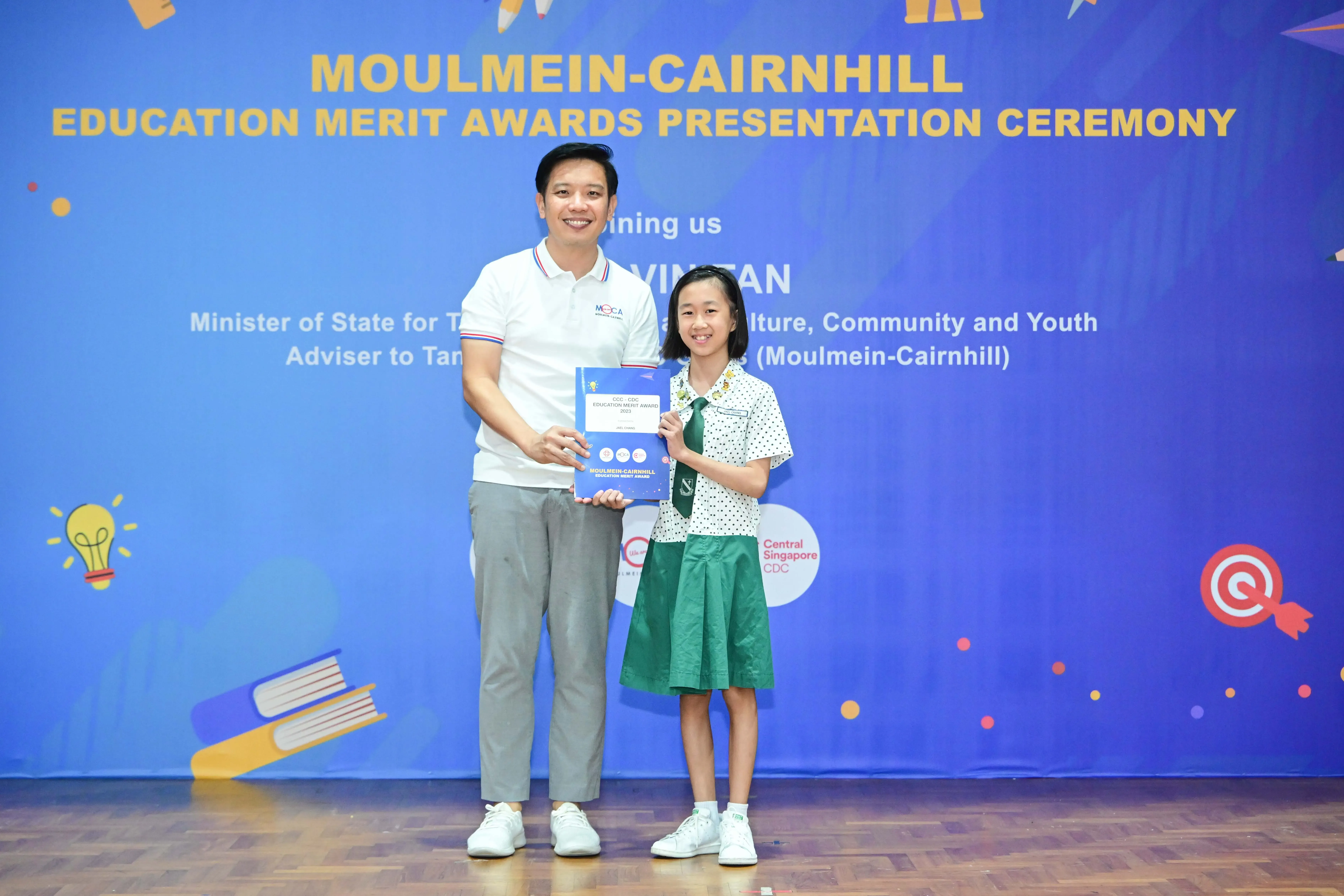 A man and a young girl in school uniform hold a certificate at the Moulmein-Cairnhill Education Merit Awards ceremony.