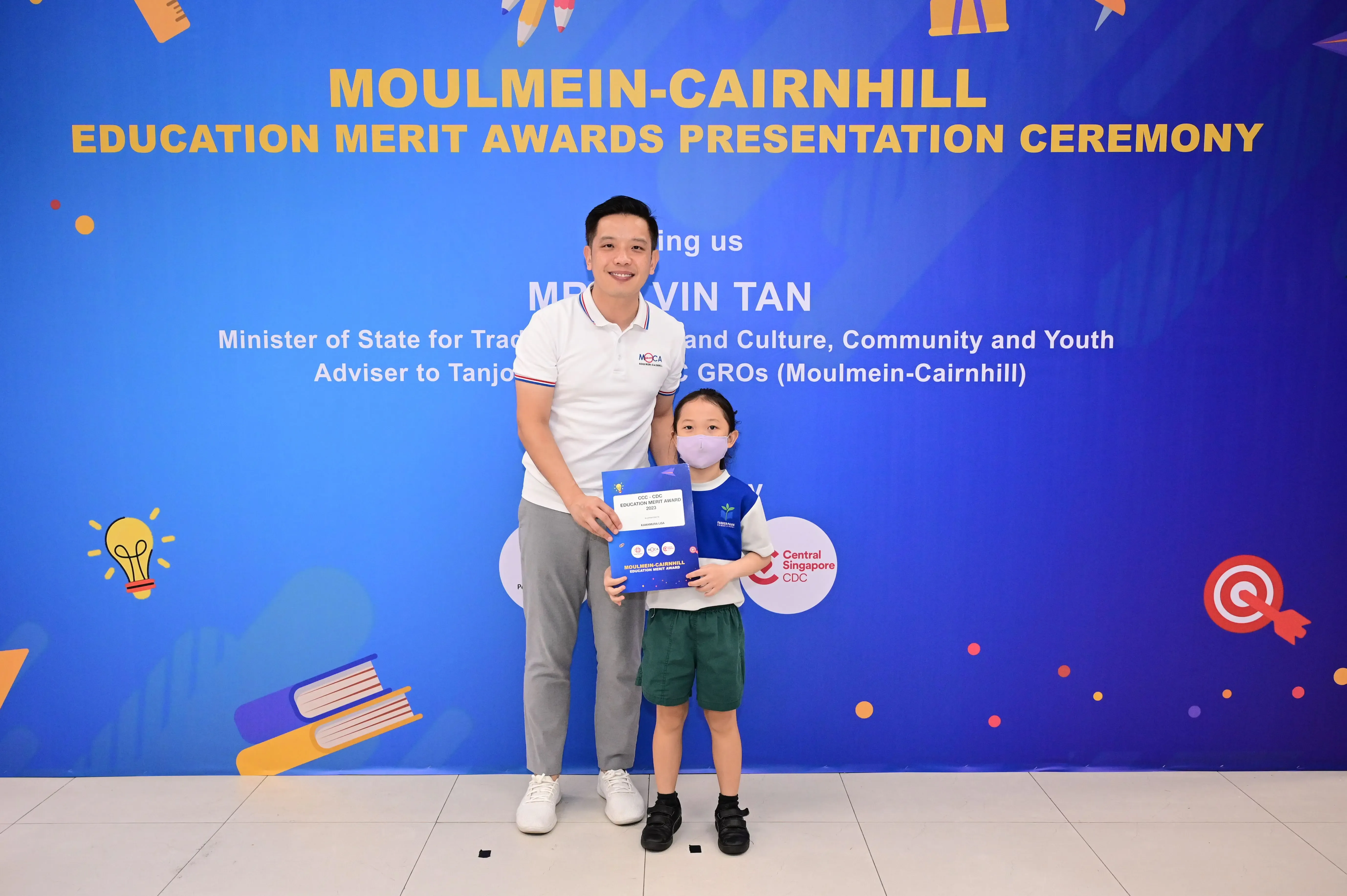 Man and masked child holding an award folder at the Moulmein-Cairnhill Education Merit Awards Presentation Ceremony.