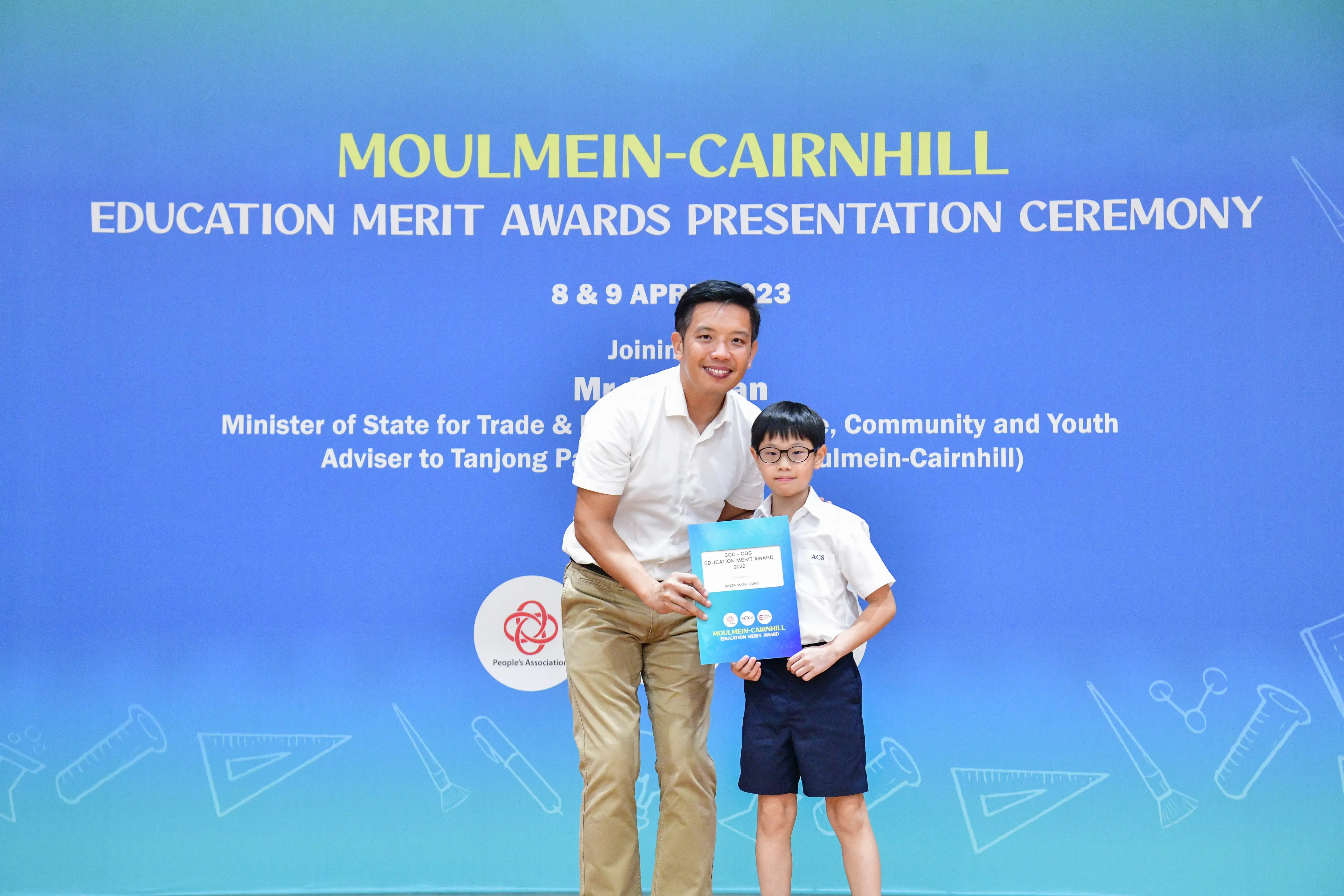 A man and a young boy hold an award certificate at the Moulmein-Cairnhill Education Merit Awards Ceremony, April 2023.