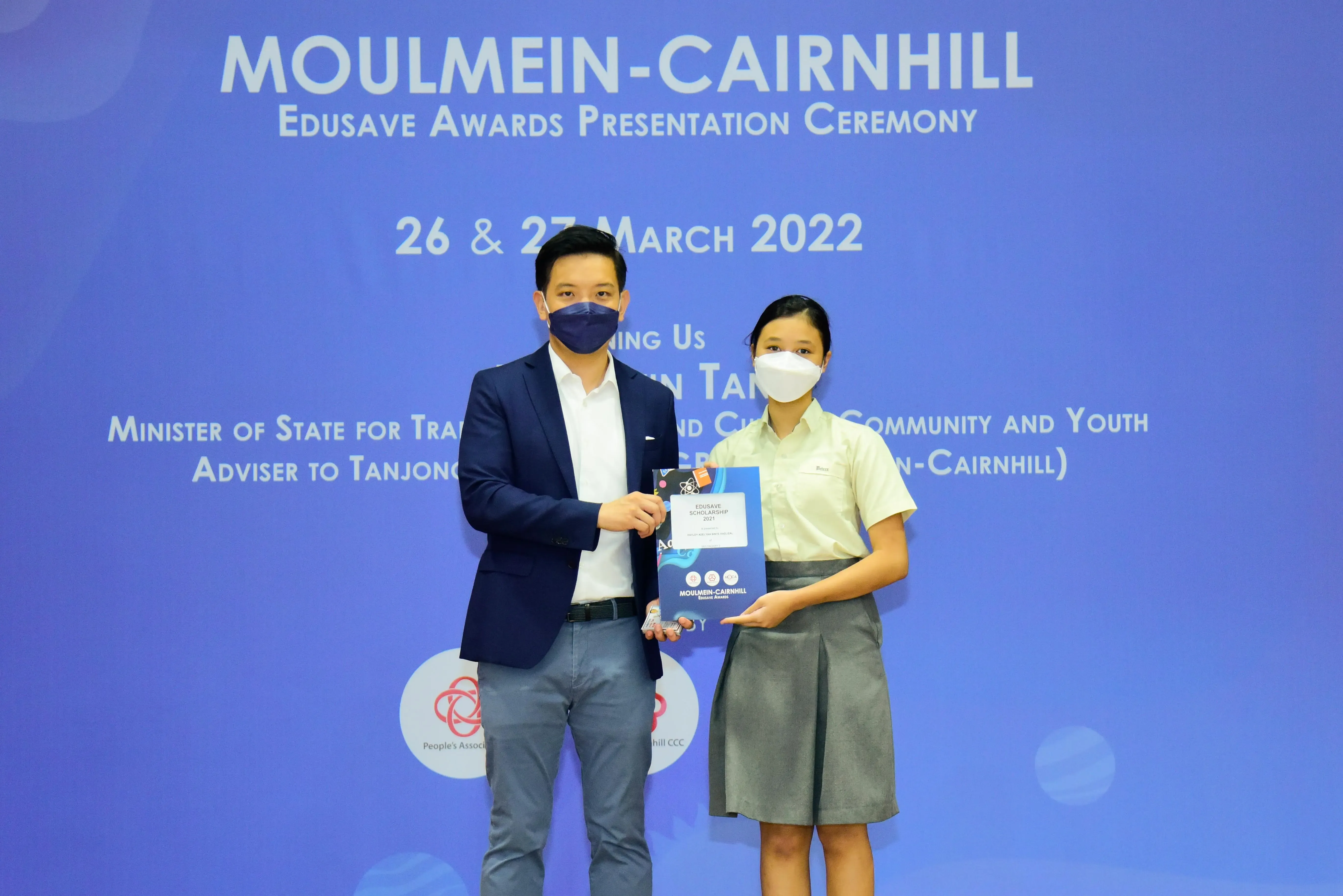 Two masked people hold an award booklet at the Moulmein-Cairnhill Edusave Awards Presentation Ceremony, March 2022.