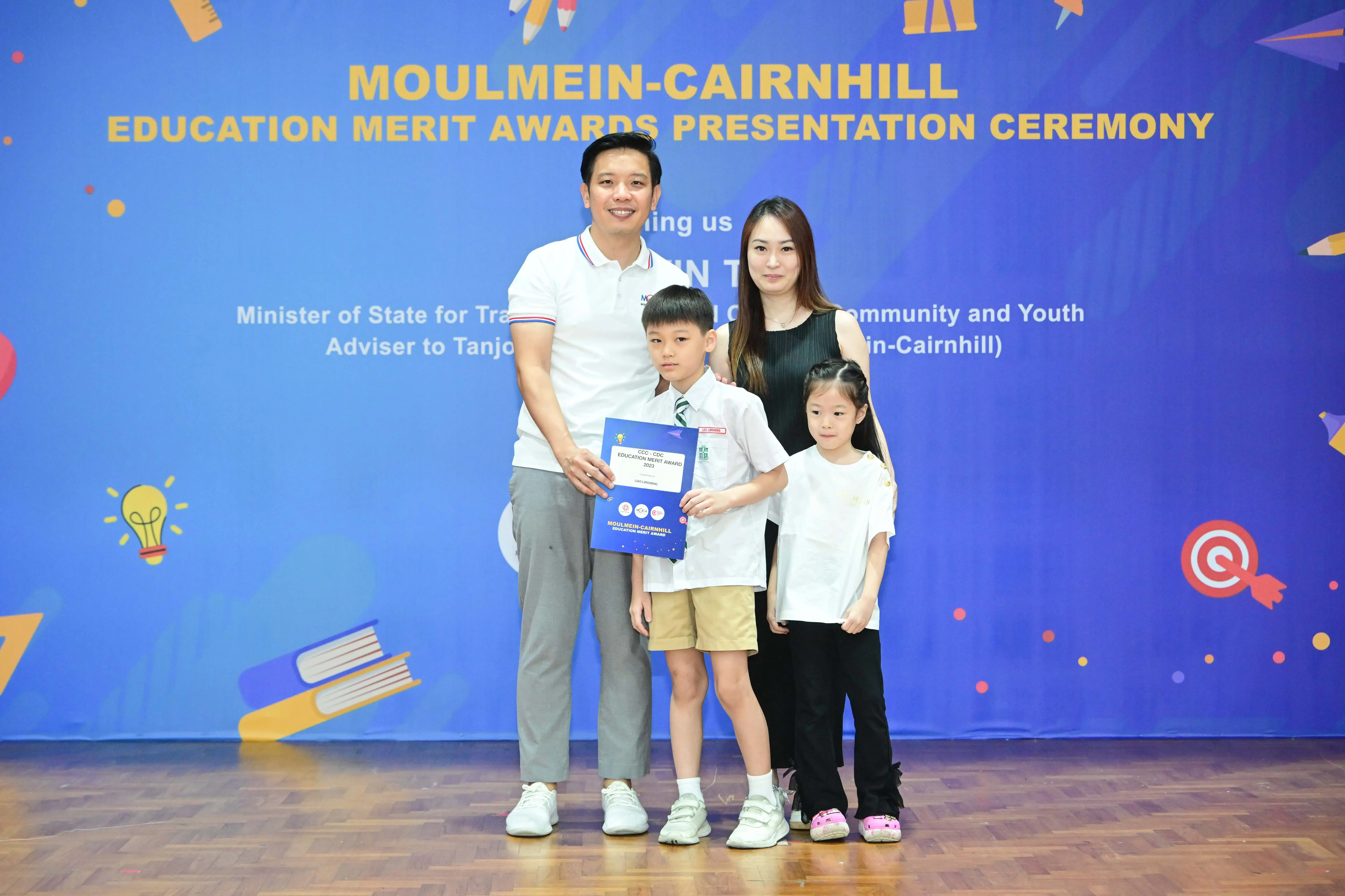 Family of four poses at Moulmein-Cairnhill Education Merit Awards ceremony, boy holding a blue award certificate.