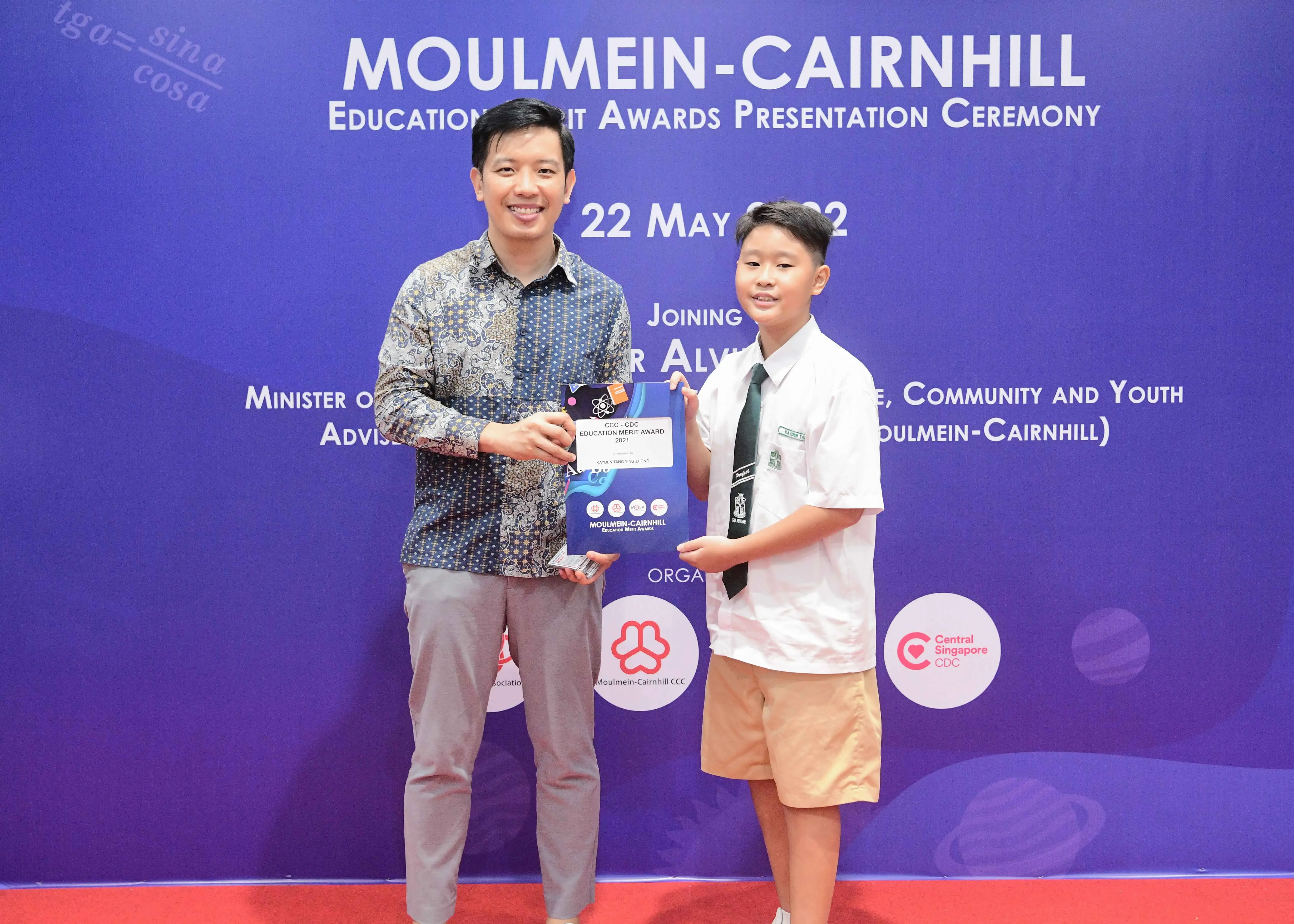 An adult and a young student hold an award together at the Moulmein-Cairnhill Education Merit Awards Ceremony on 22 May 2022.