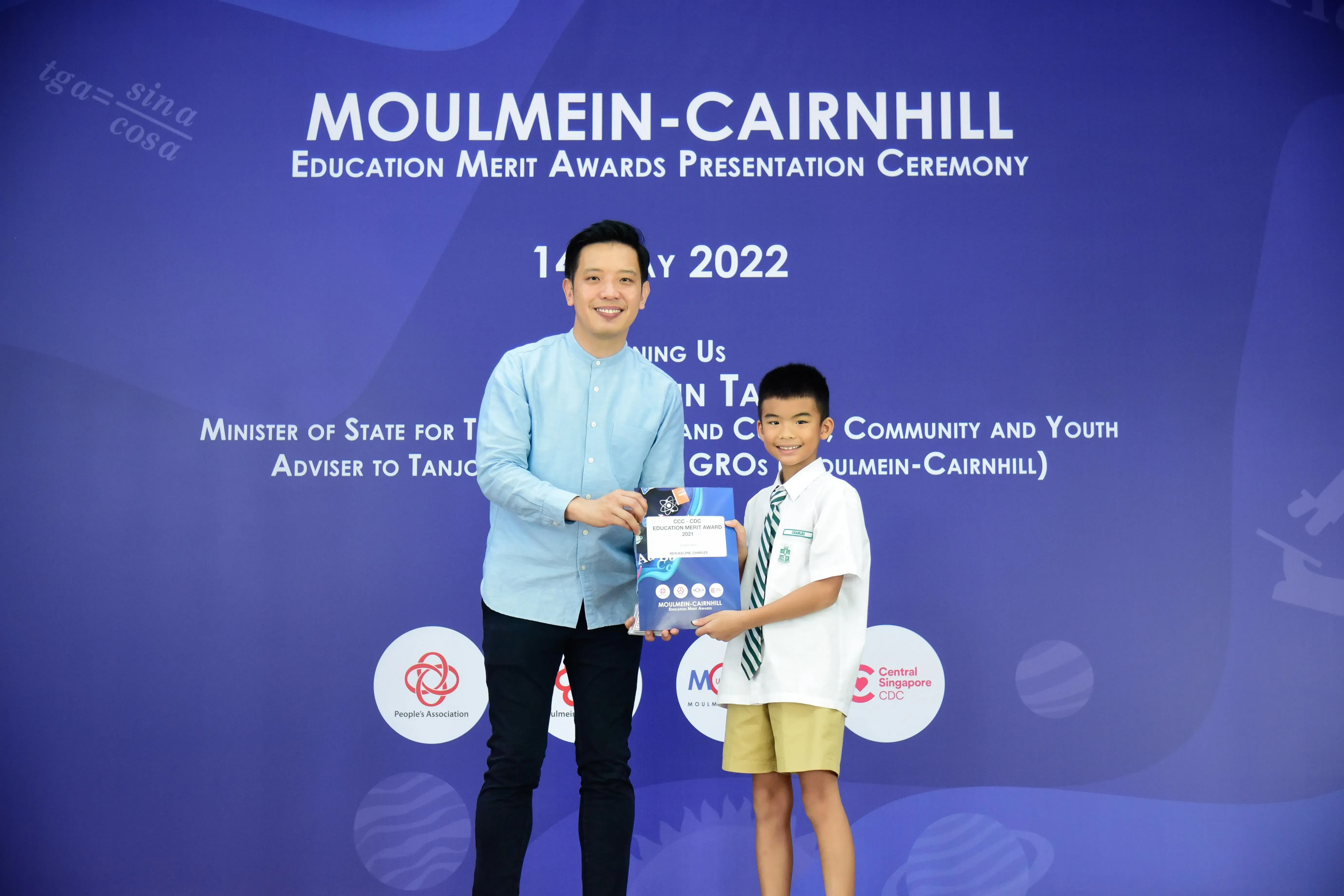 An adult and a young boy hold an award together at the Moulmein-Cairnhill Education Merit Awards Ceremony 2022.