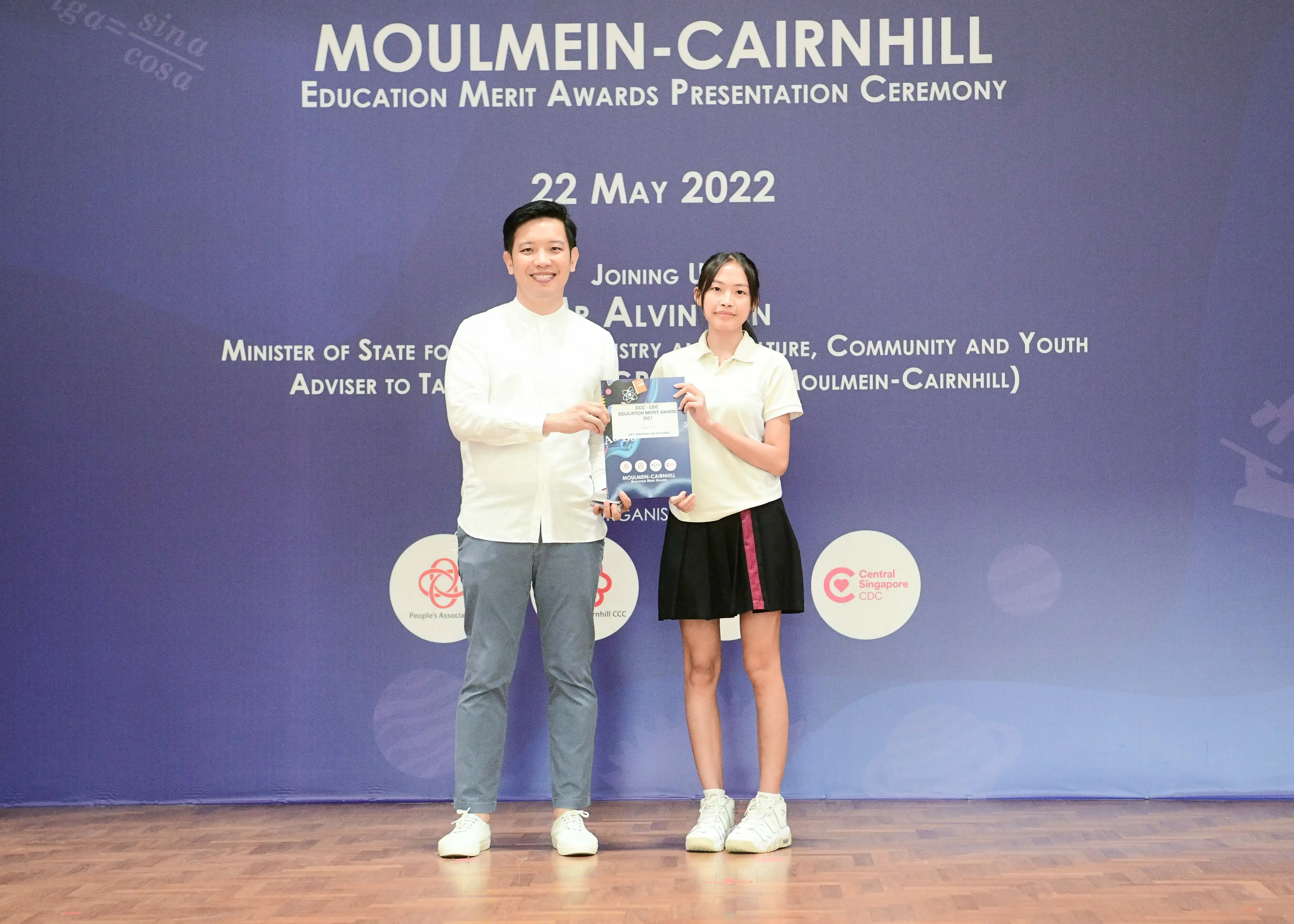 Two people stand holding a booklet at the Moulmein-Cairnhill Education Merit Awards Ceremony on 22 May 2022.