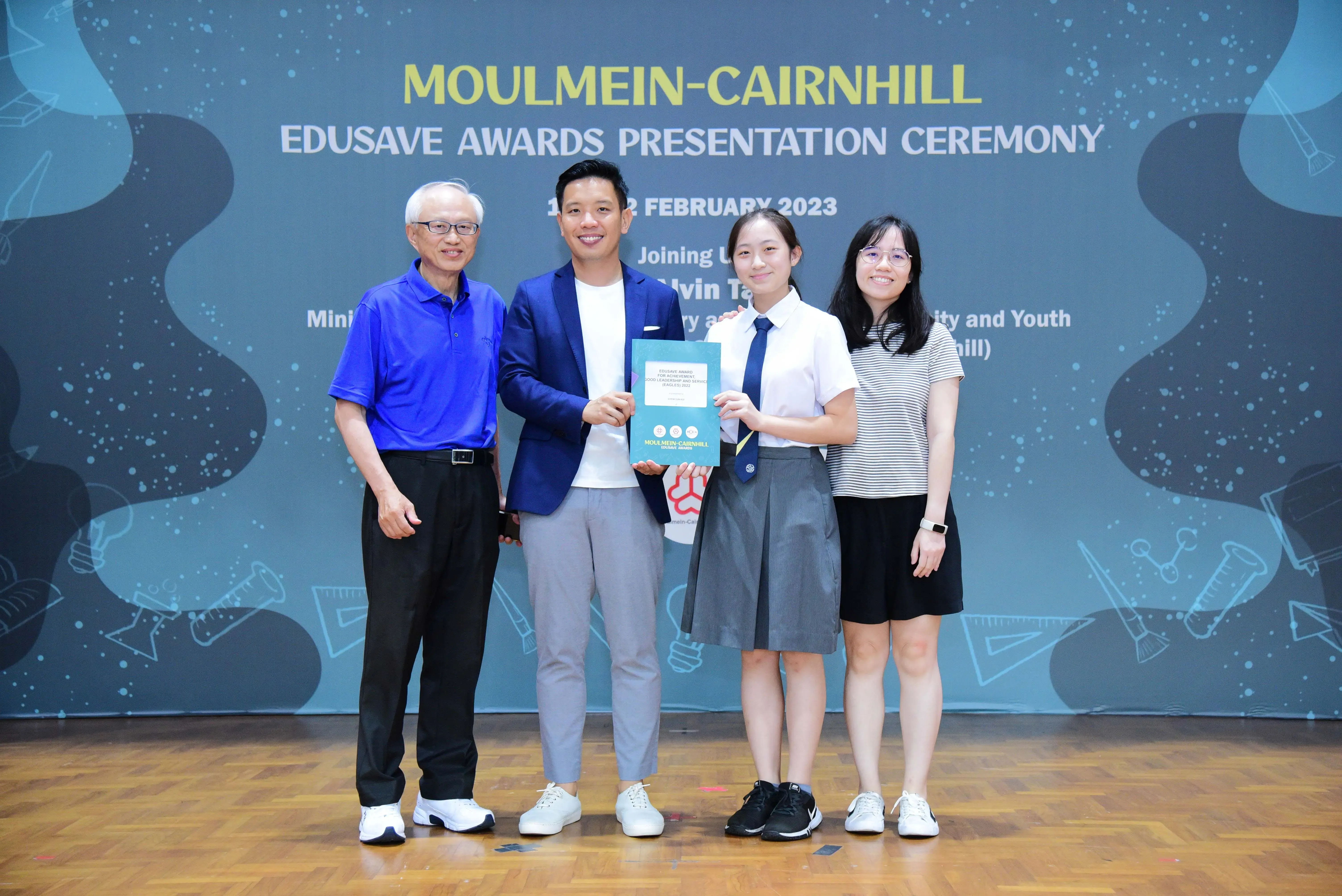 Four people pose on a stage at the Moulmein-Cairnhill Edusave Awards Presentation Ceremony in February 2023.