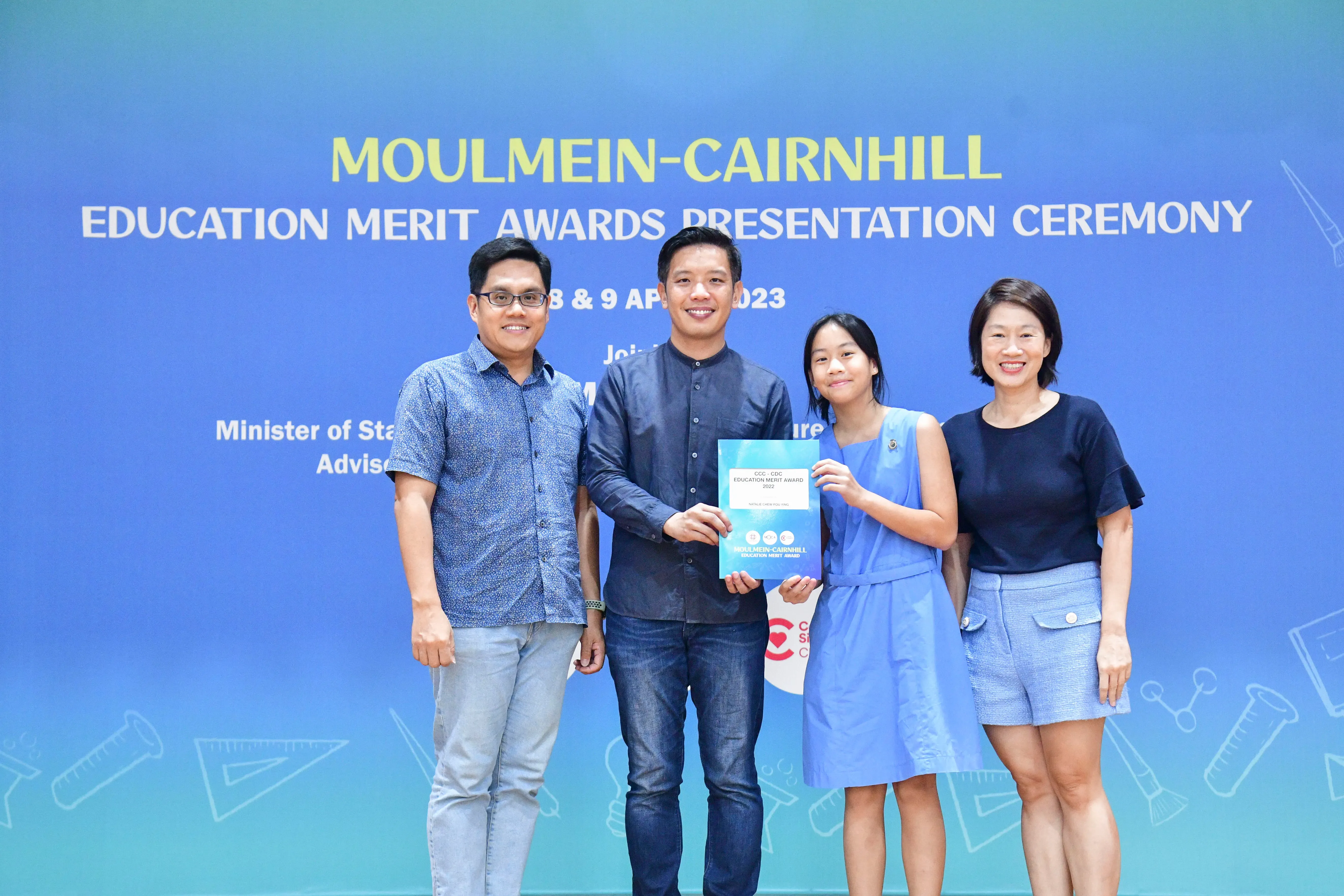 Four people pose at the Moulmein-Cairnhill Education Merit Awards Presentation Ceremony, holding a certificate.