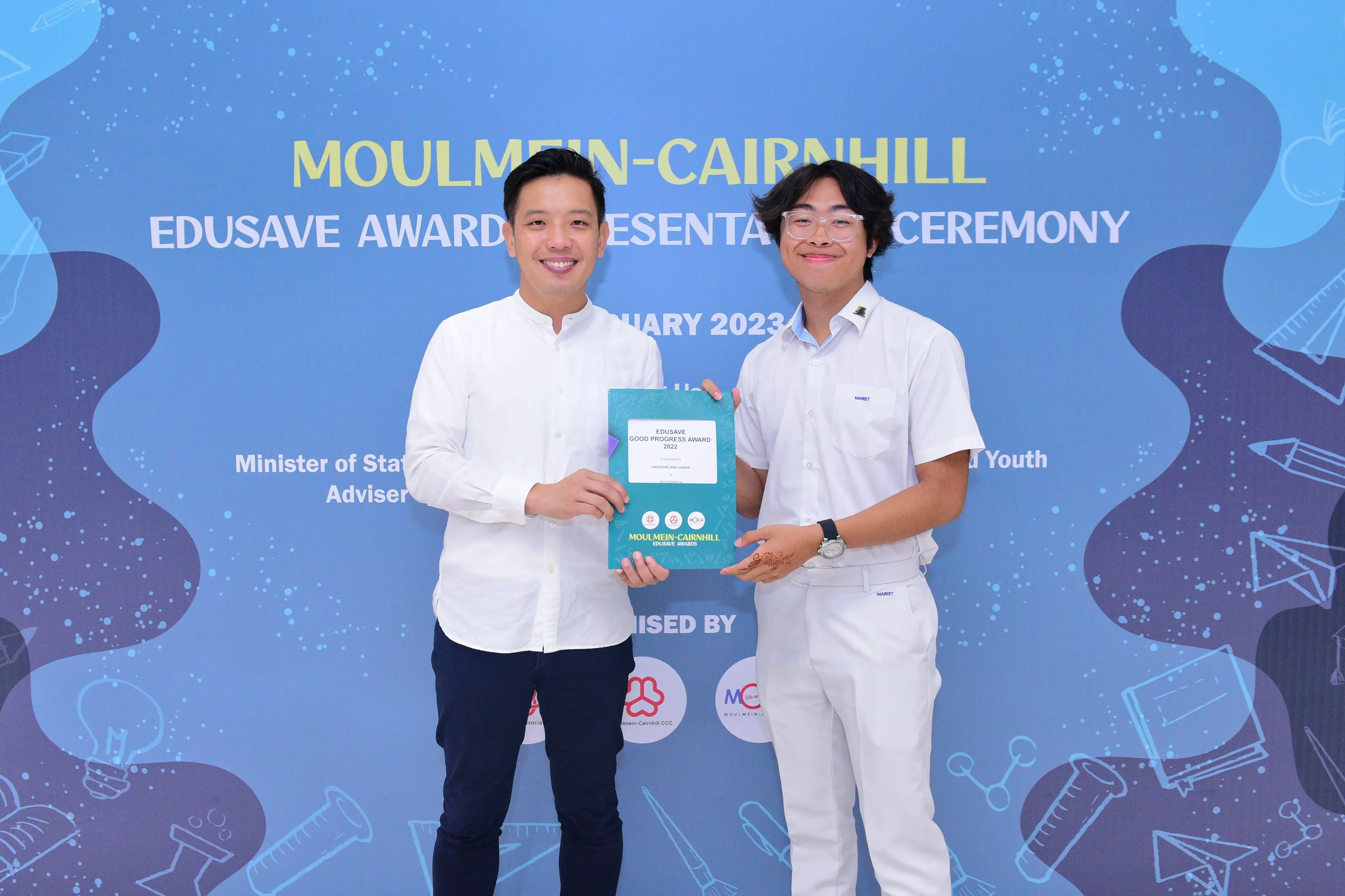 Two smiling men hold an Edusave Good Progress Award certificate at the Moulmein-Cairnhill Awards Ceremony 2023.