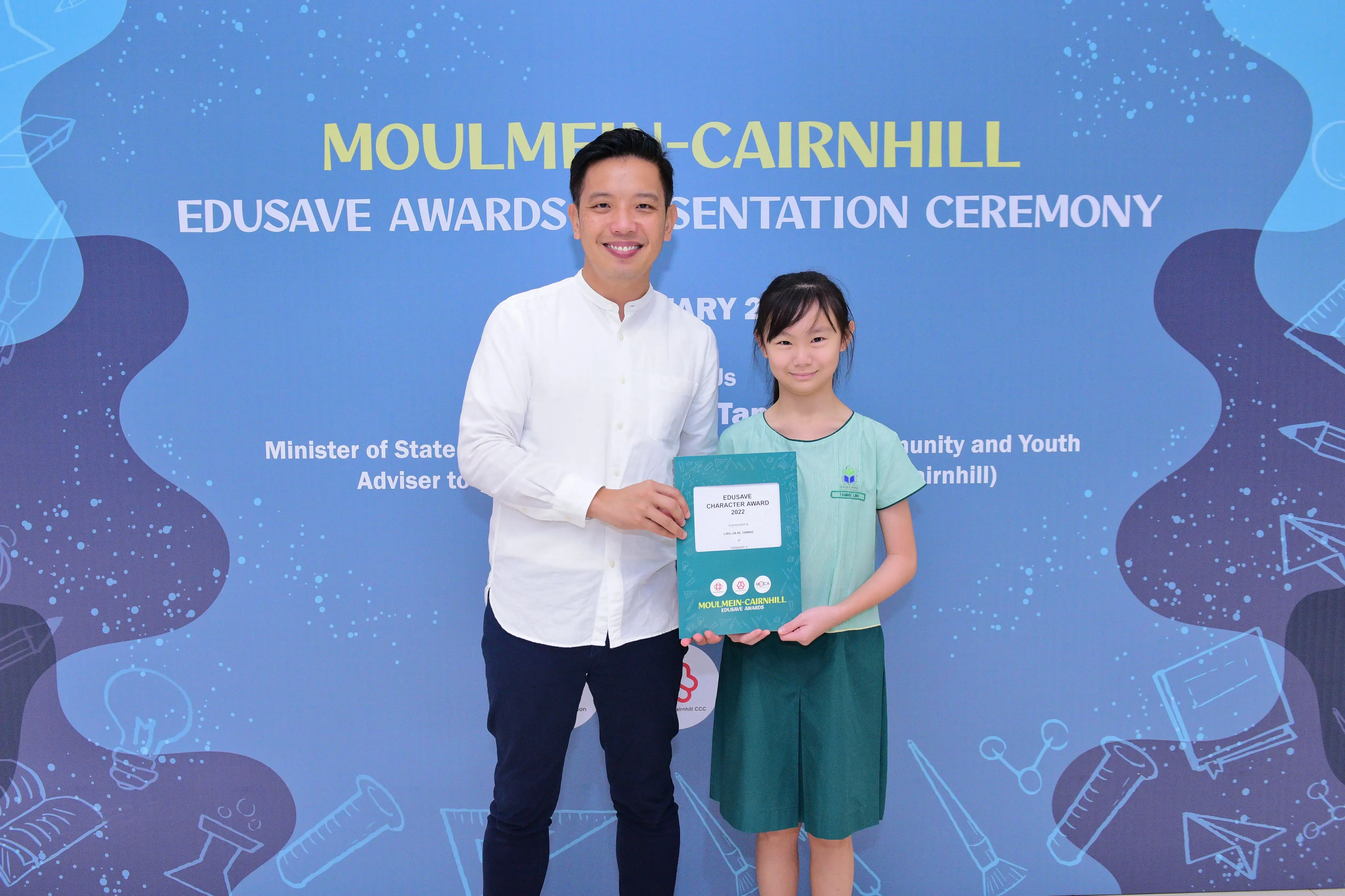 A man and a young girl hold an Edusave Character Award certificate at the Moulmein-Cairnhill Edusave Awards Ceremony.