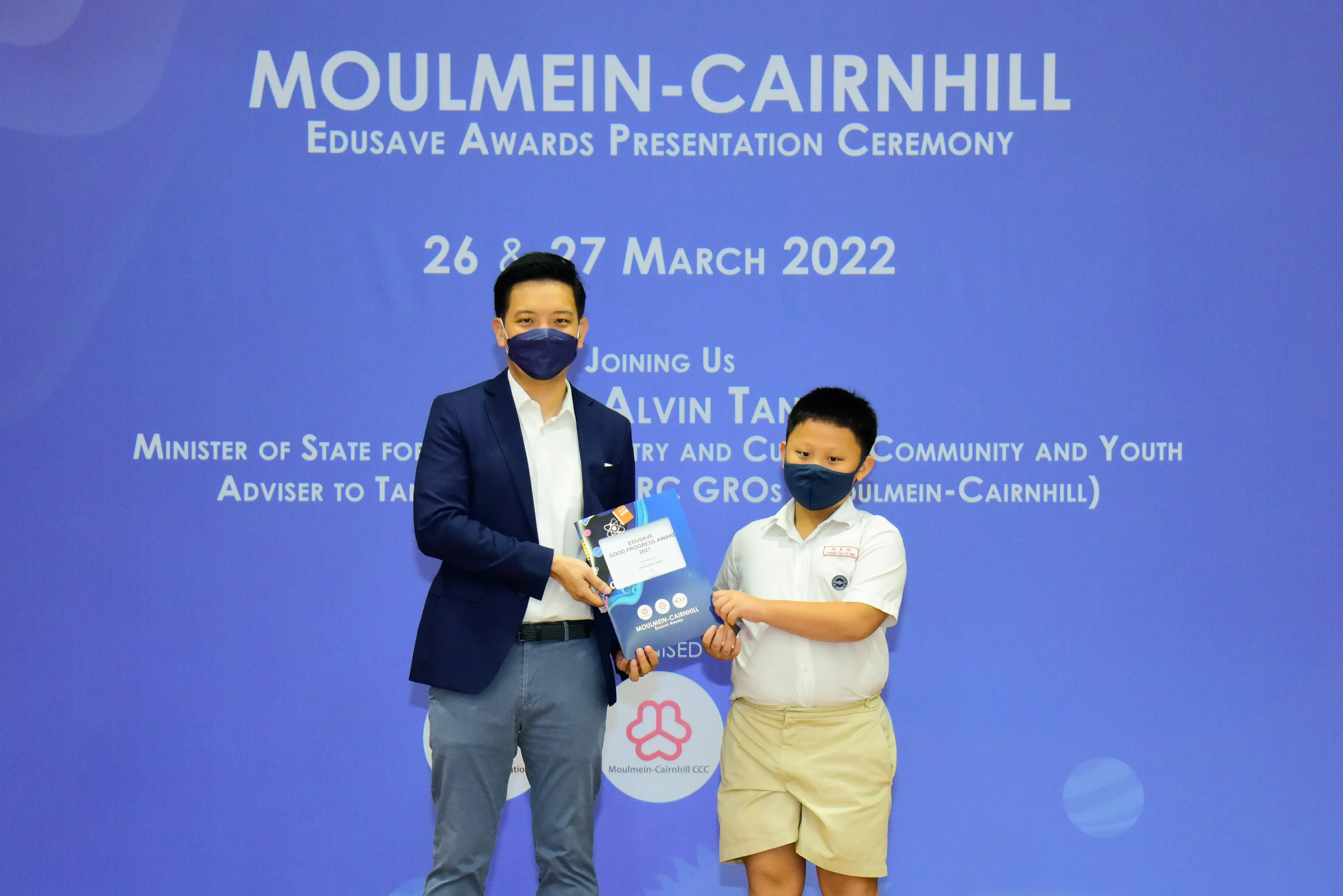 An adult in a blazer presents an award to a young student in uniform at the Moulmein-Cairnhill Edusave ceremony.
