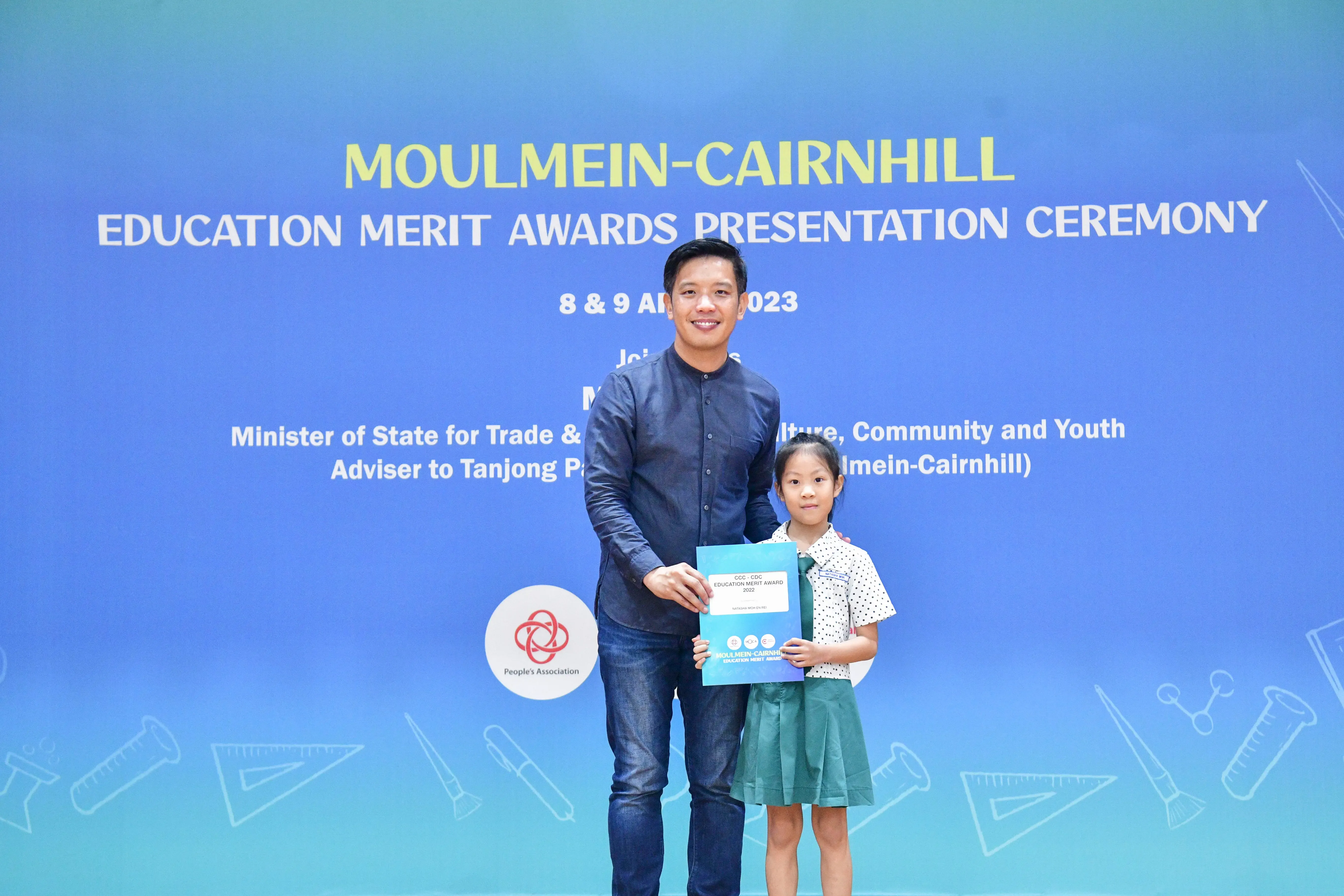 A man and a young girl hold a certificate together at the Moulmein-Cairnhill Education Merit Awards Ceremony 2023.