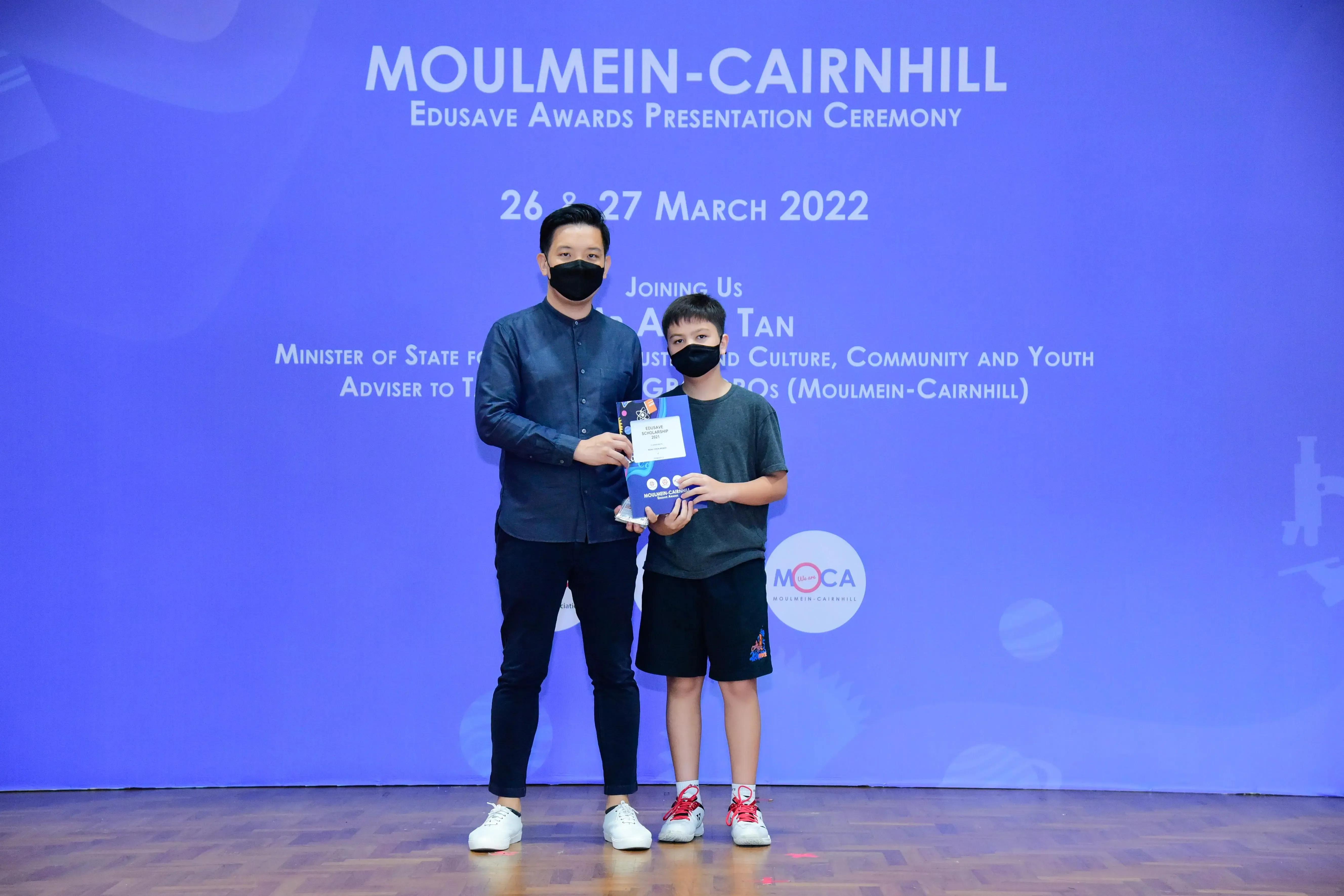 An adult and a child wearing masks hold an award at the Moulmein-Cairnhill Edusave Awards Ceremony, March 2022.