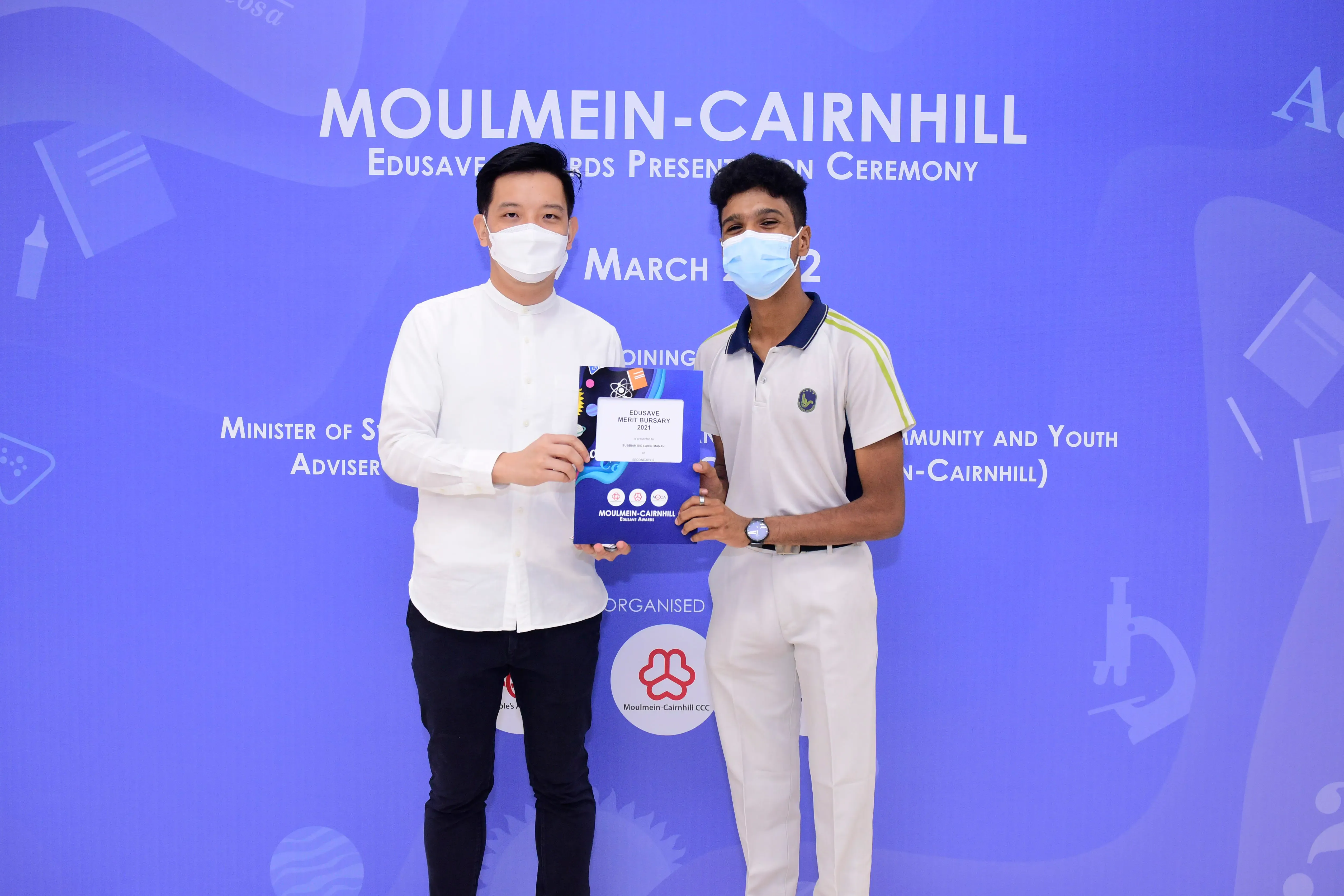 Two masked men hold an Edusave Merit Bursary award at the Moulmein-Cairnhill Awards Presentation Ceremony.