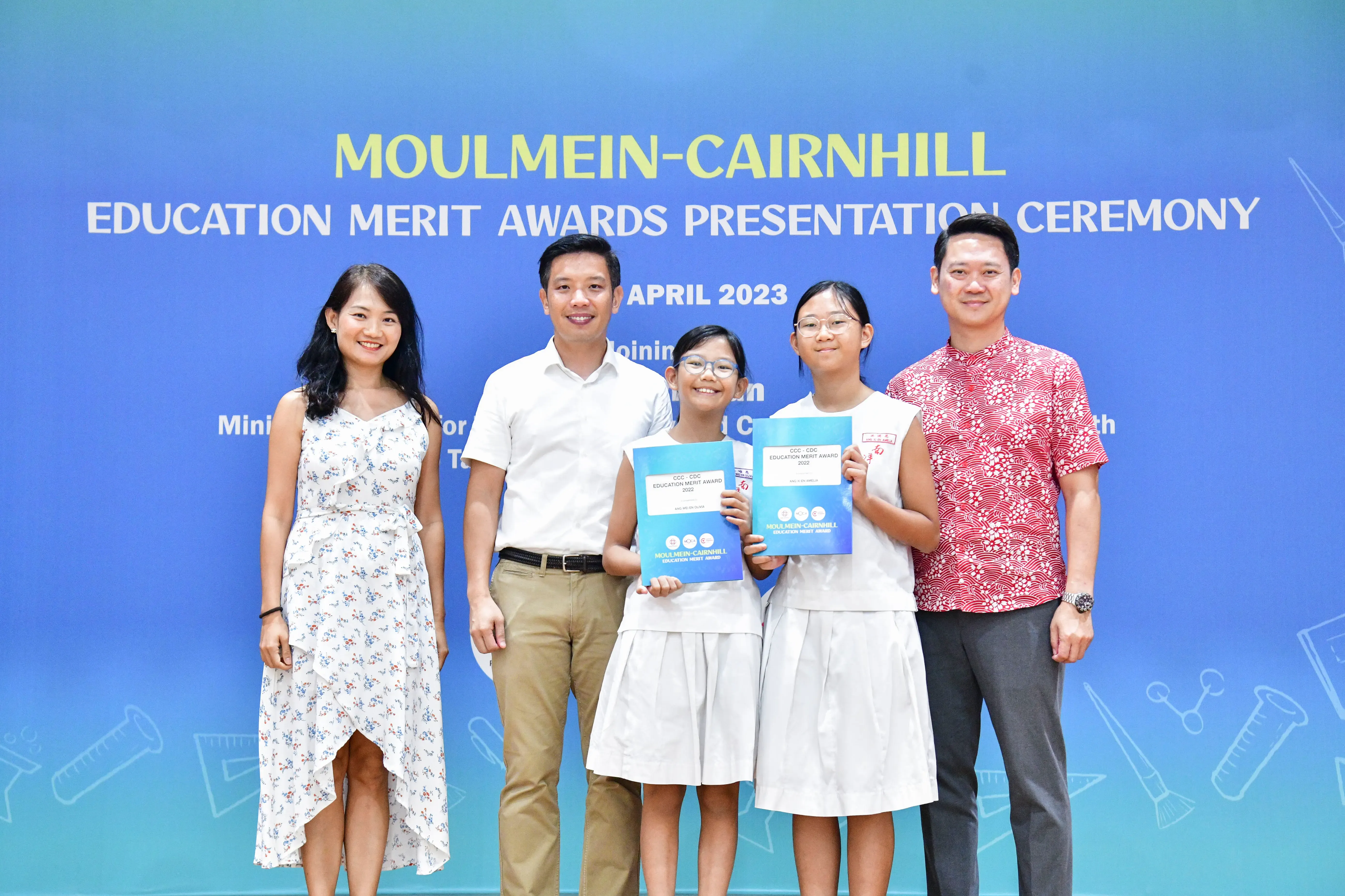 Five people pose at the Moulmein-Cairnhill Education Merit Awards Presentation Ceremony, April 2023, two girls holding award folders.