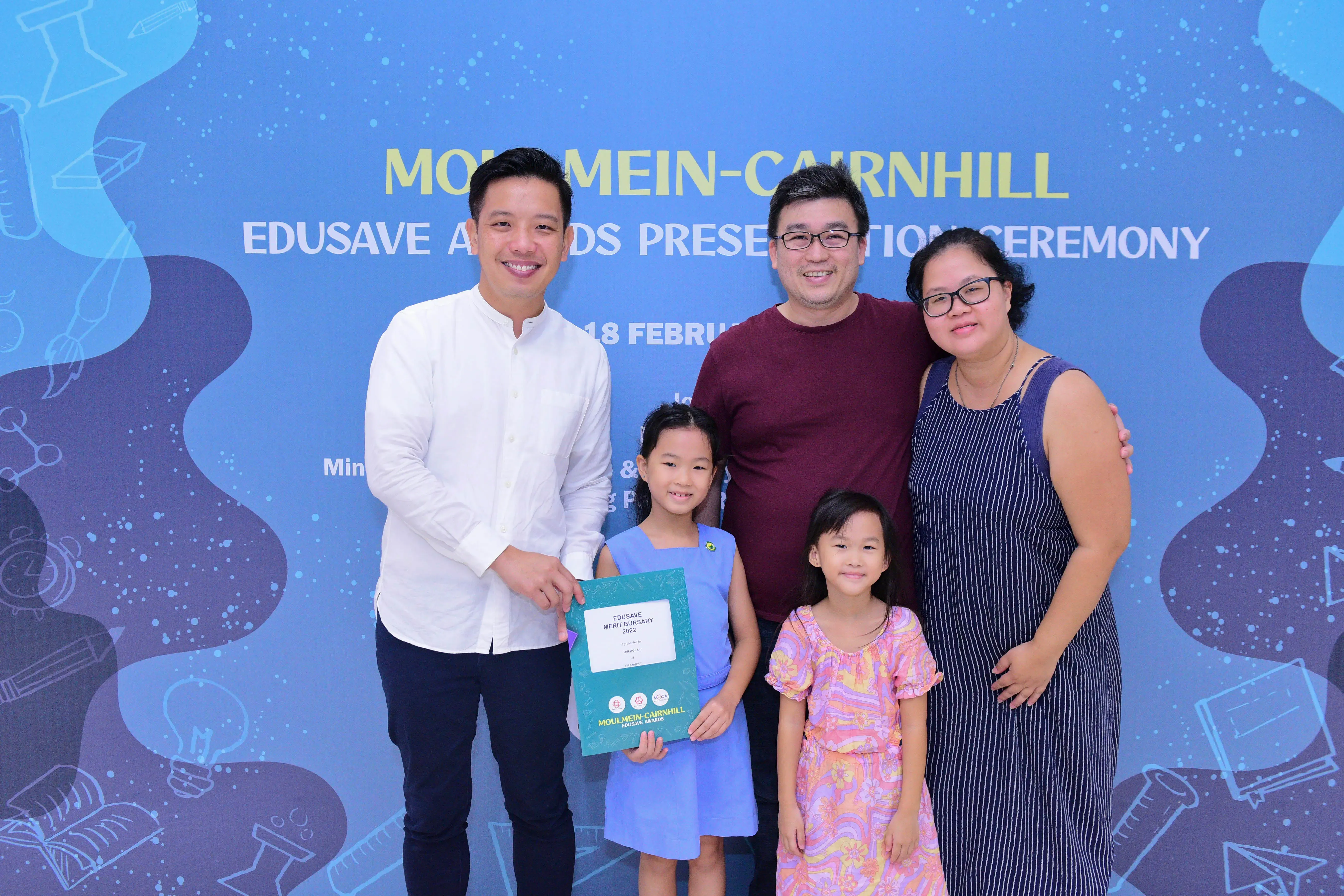 Five people pose at the Moulmein-Cairnhill Edusave Awards Presentation Ceremony, with a girl holding a certificate.