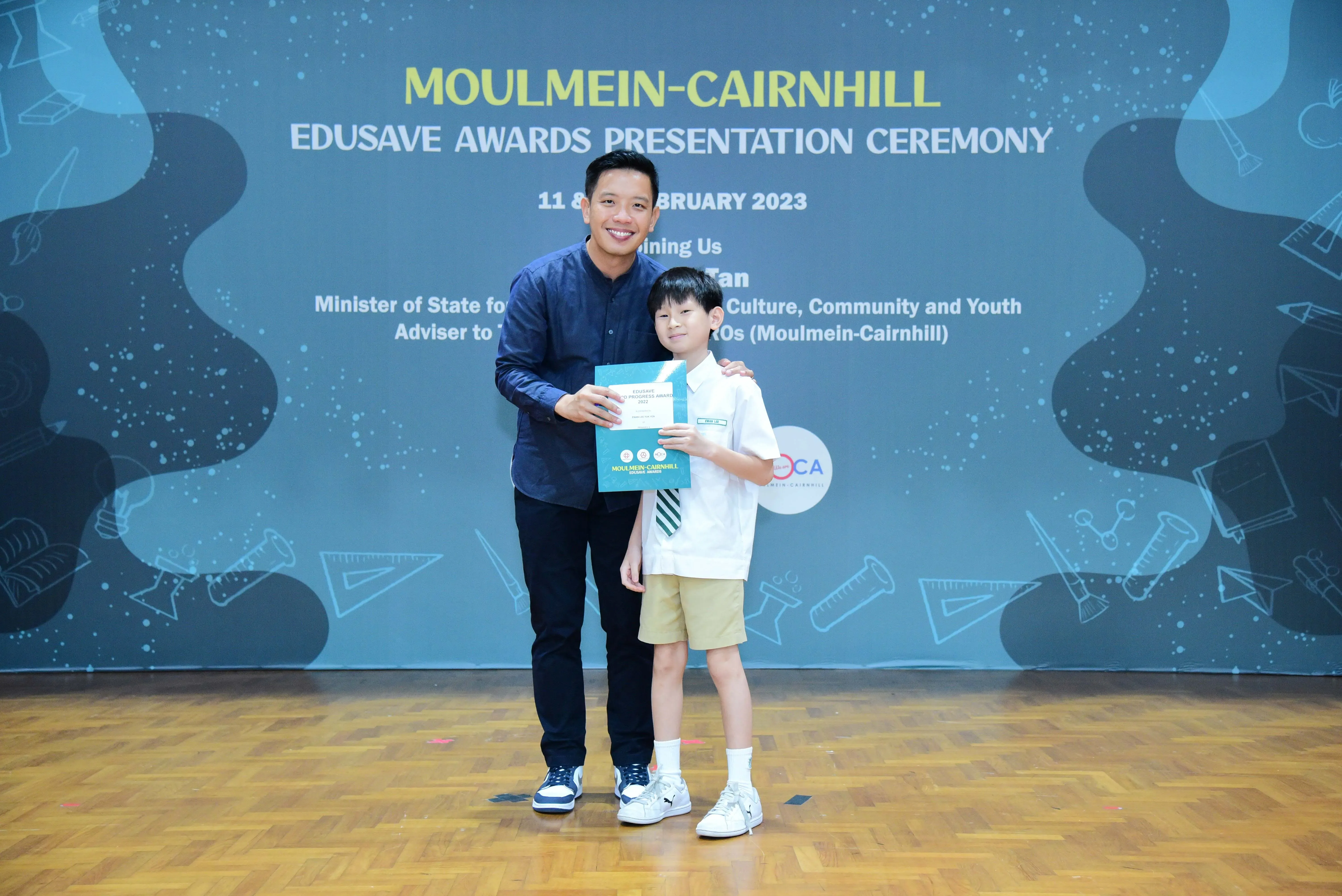 Adult man and young boy hold a certificate together at Moulmein-Cairnhill Edusave Awards Ceremony, February 2023.