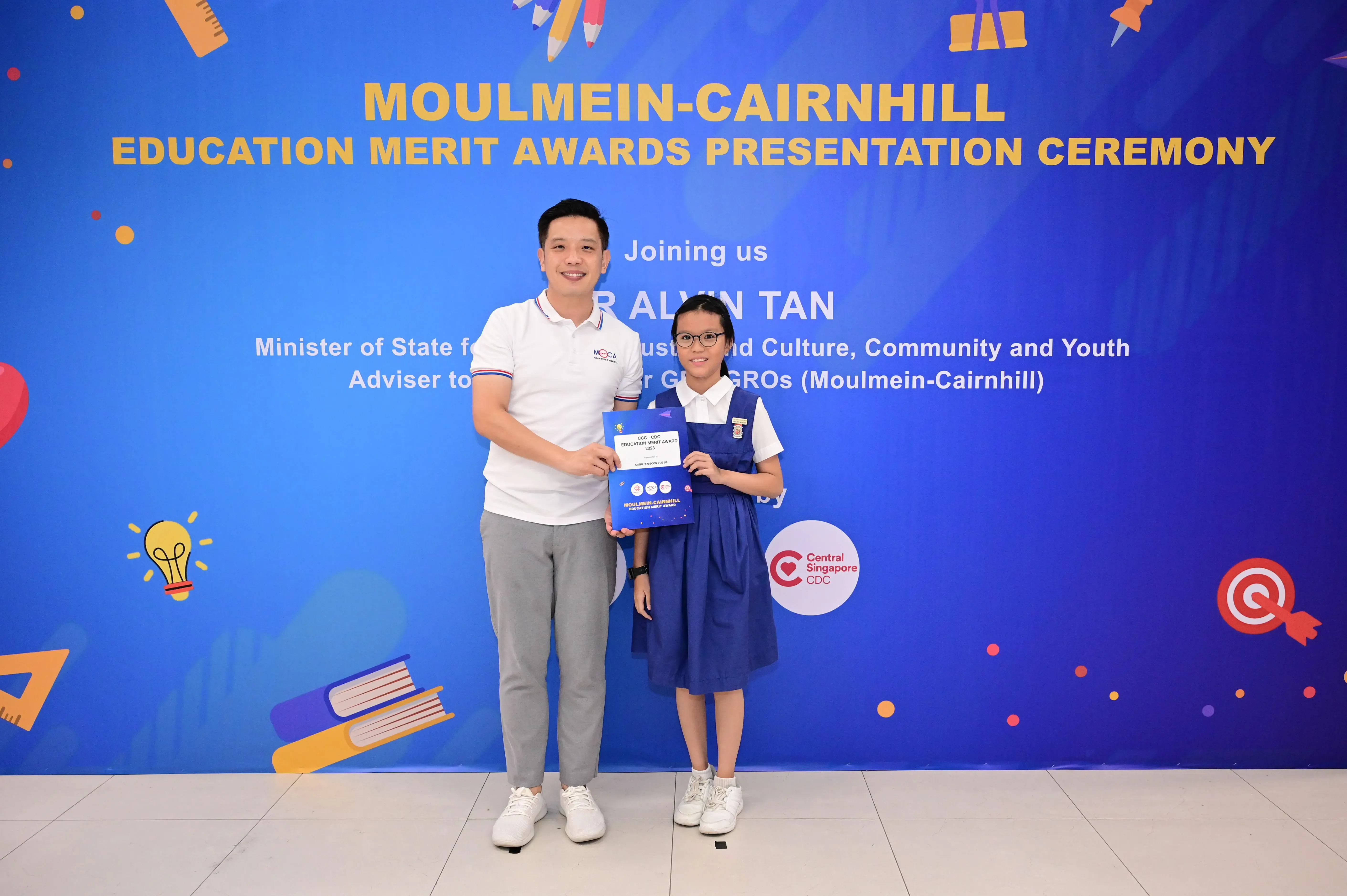 A man and a young girl holding an award certificate at the Moulmein-Cairnhill Education Merit Awards ceremony.