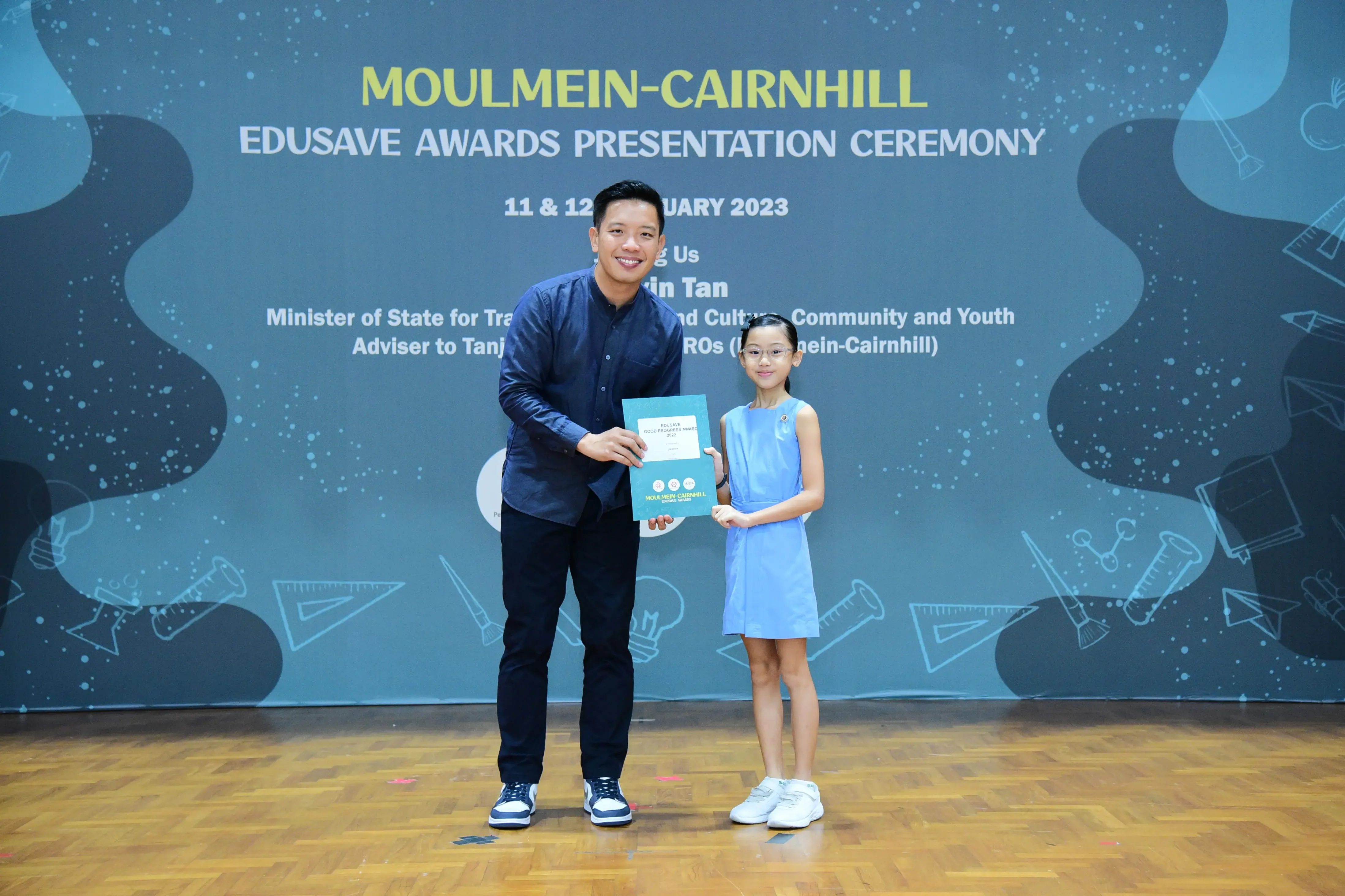 A man and a young girl hold a certificate together at the Moulmein-Cairnhill Edusave Awards Ceremony 2023.
