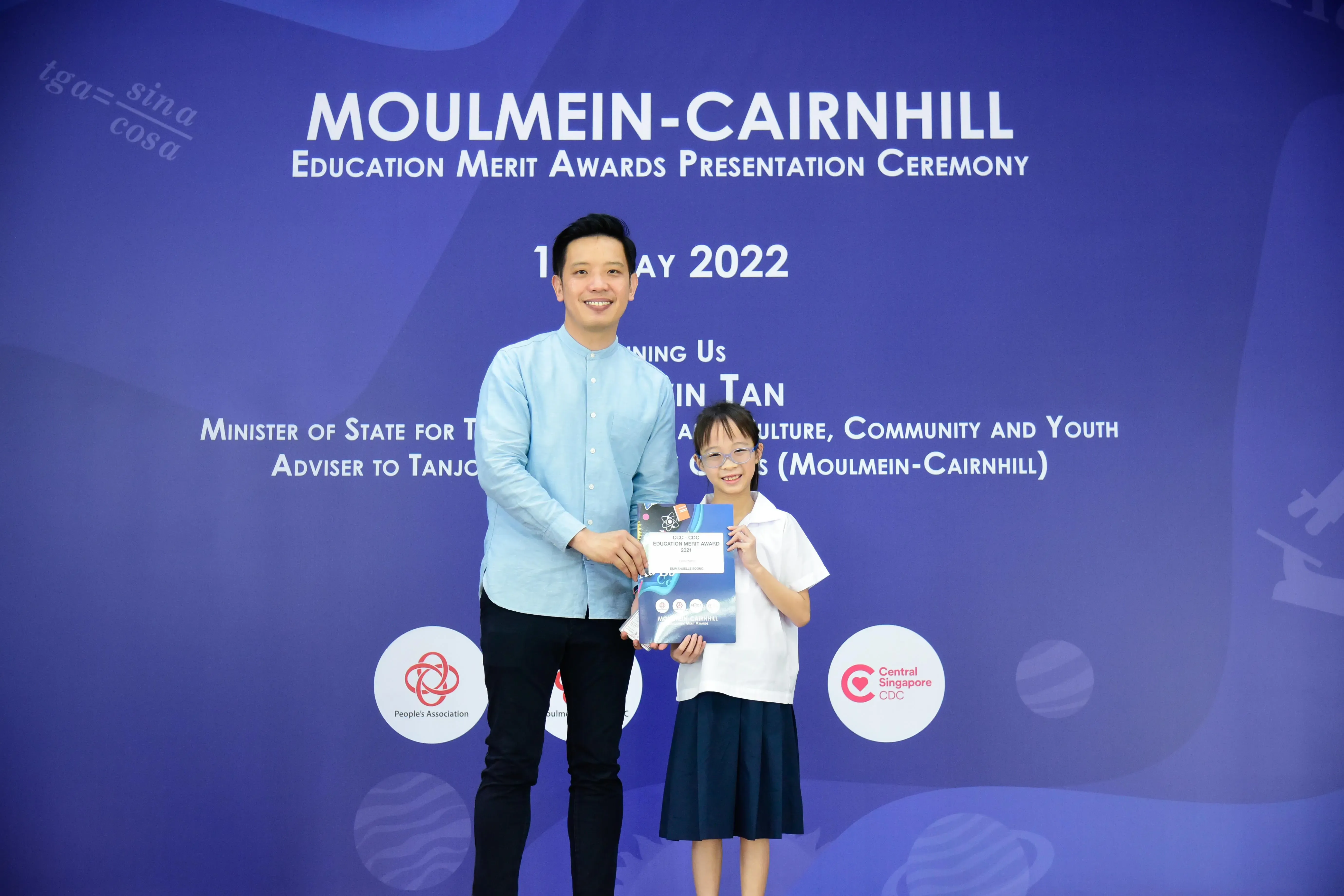 A man and a young girl hold an award certificate at the Moulmein-Cairnhill Education Merit Awards Ceremony 2022.