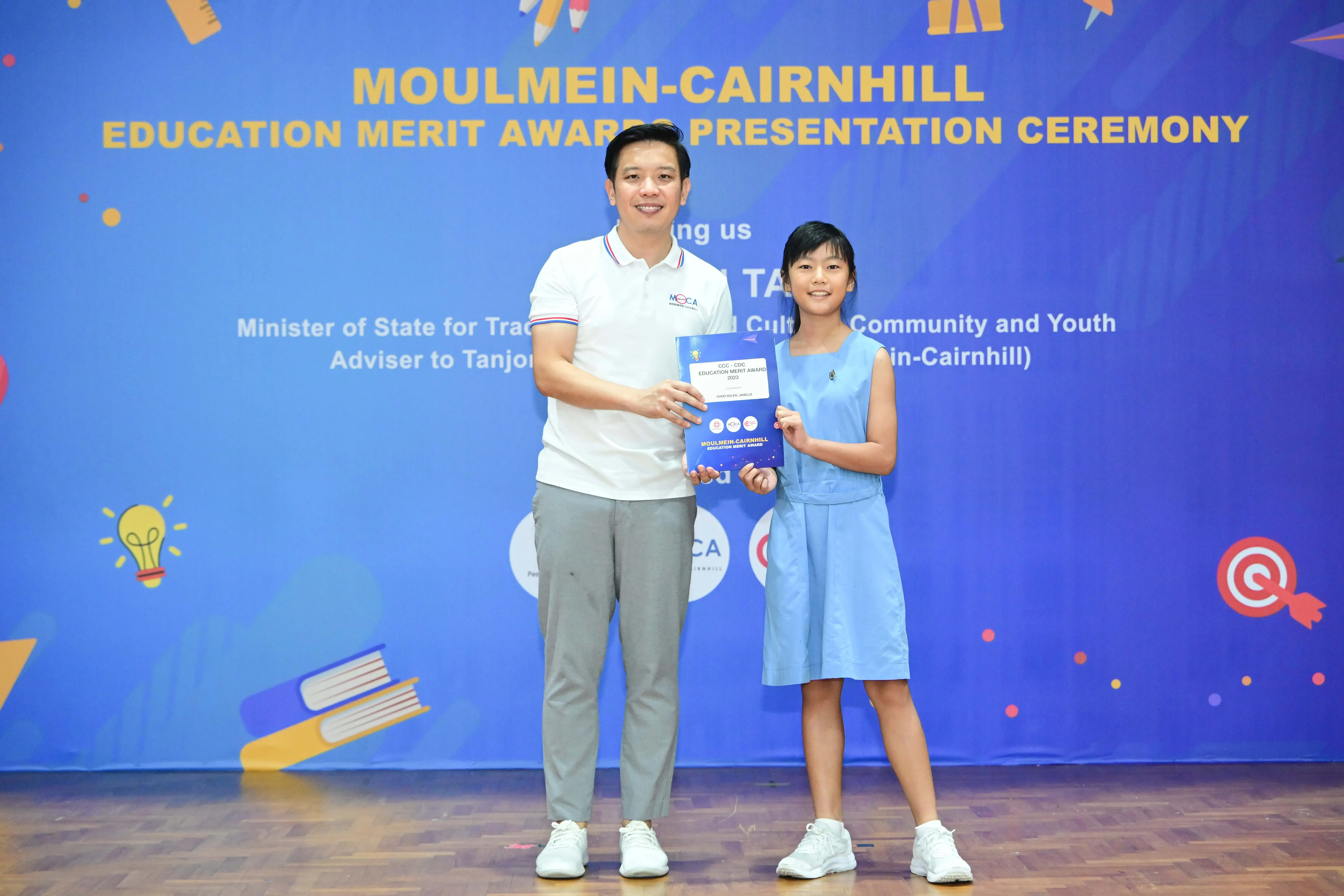 Man and young girl holding an award booklet at Moulmein-Cairnhill Education Merit Awards Presentation Ceremony.